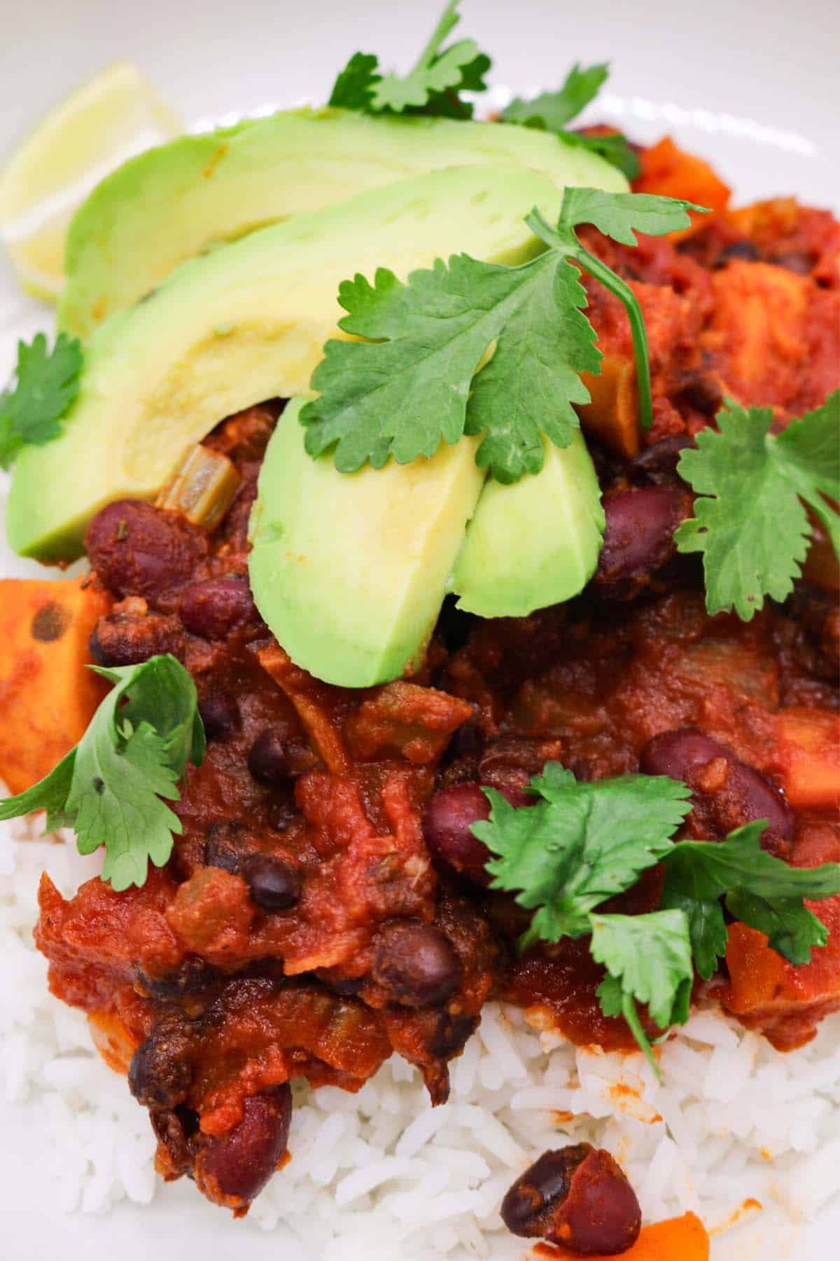 Close up of vegan chilli in a bowl with rice, avocado, lime and coriander.