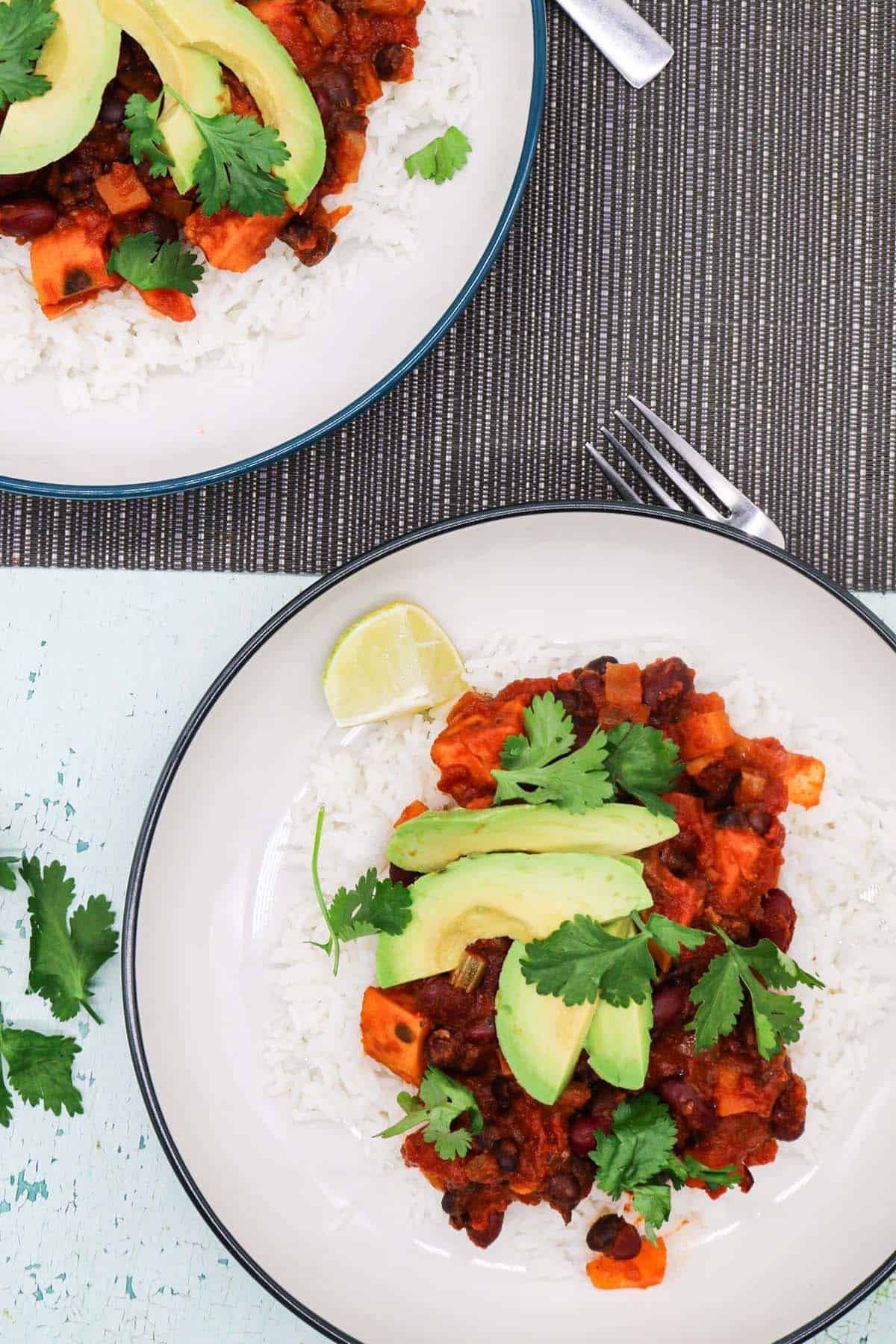Two bowls of vegan chilli with rice, avocado, lime and coriander.