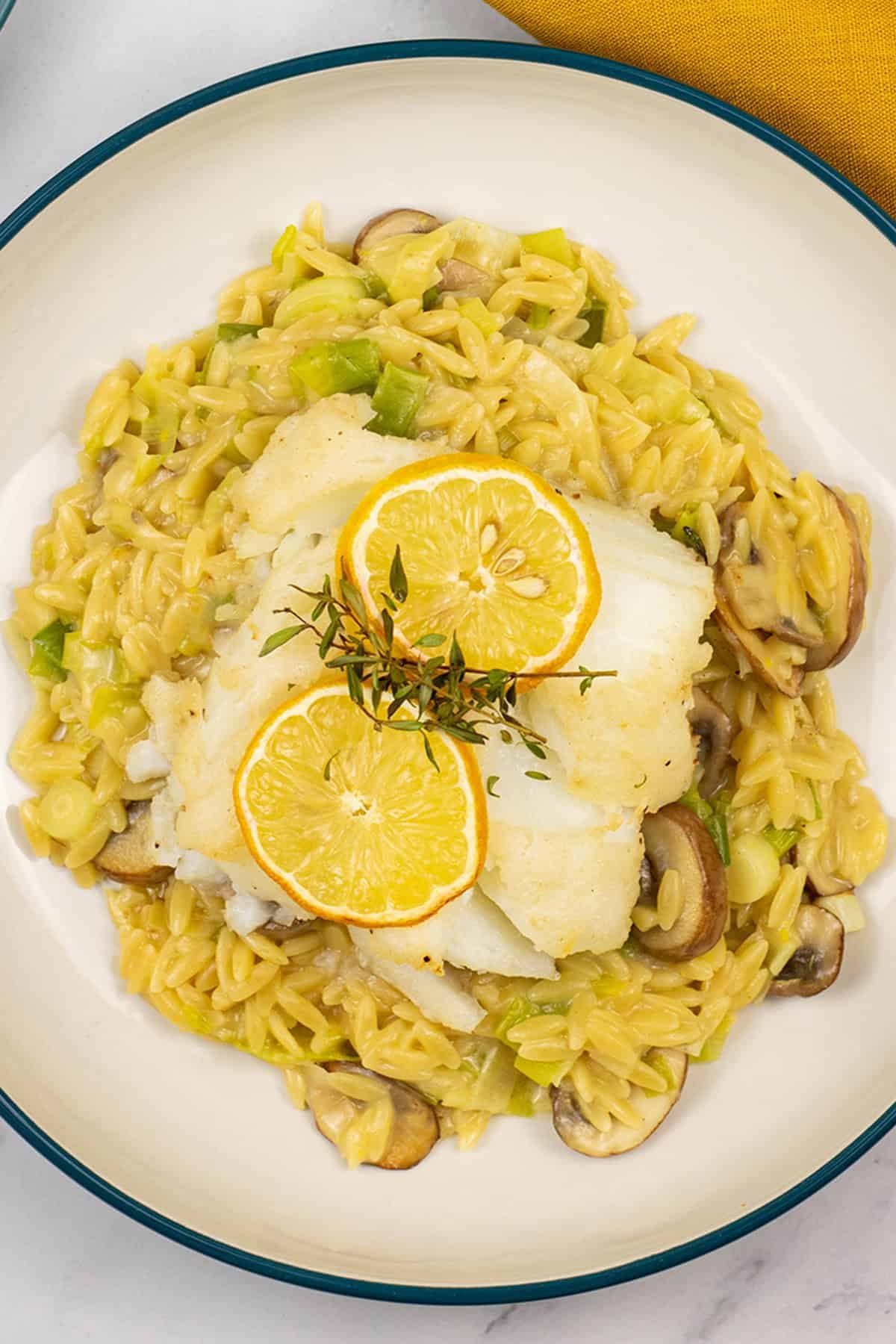 Close up of a portion of baked cod with creamy mushroom and leek orzo in a bowl.