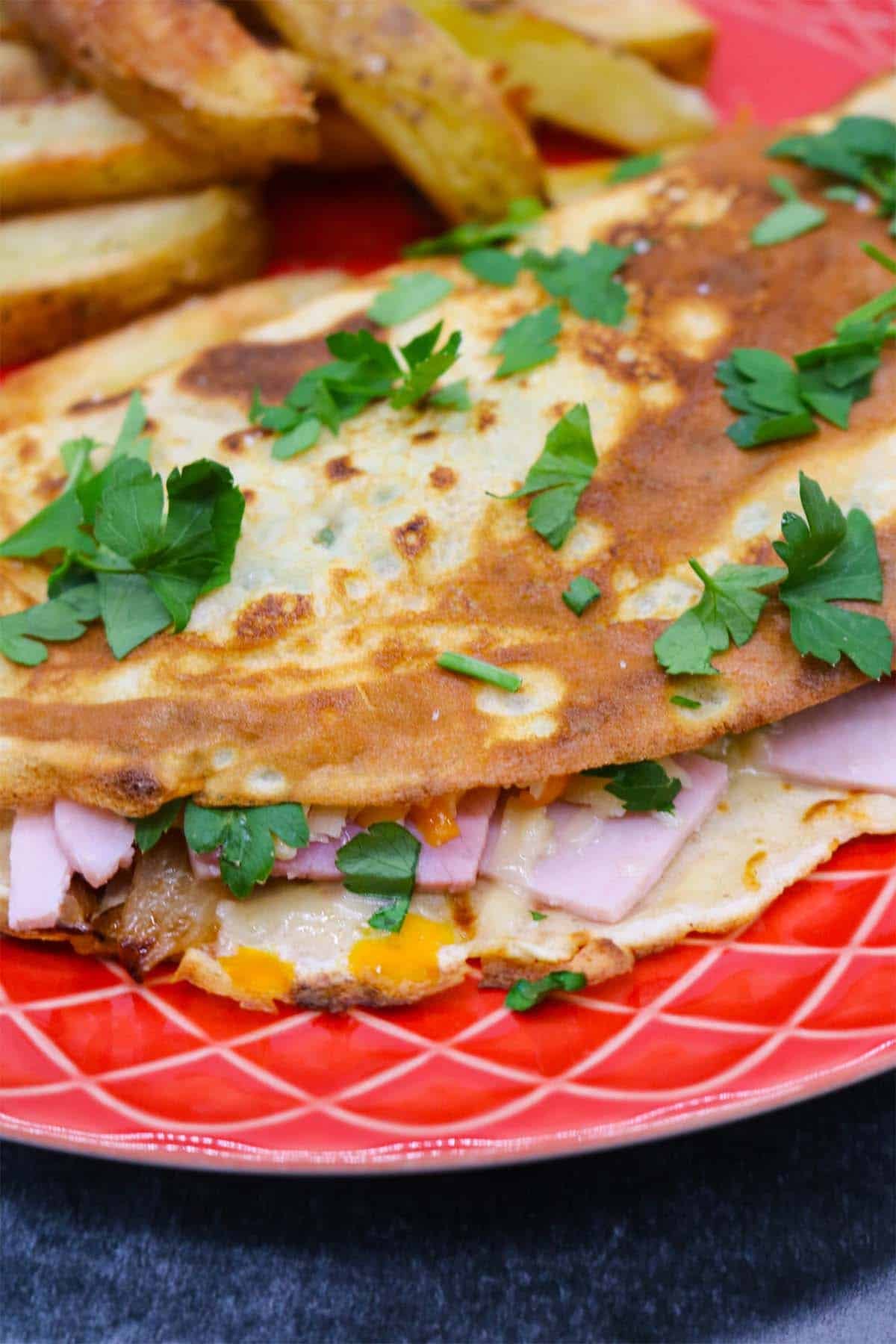 Cheese and ham pancake on red plate with chips