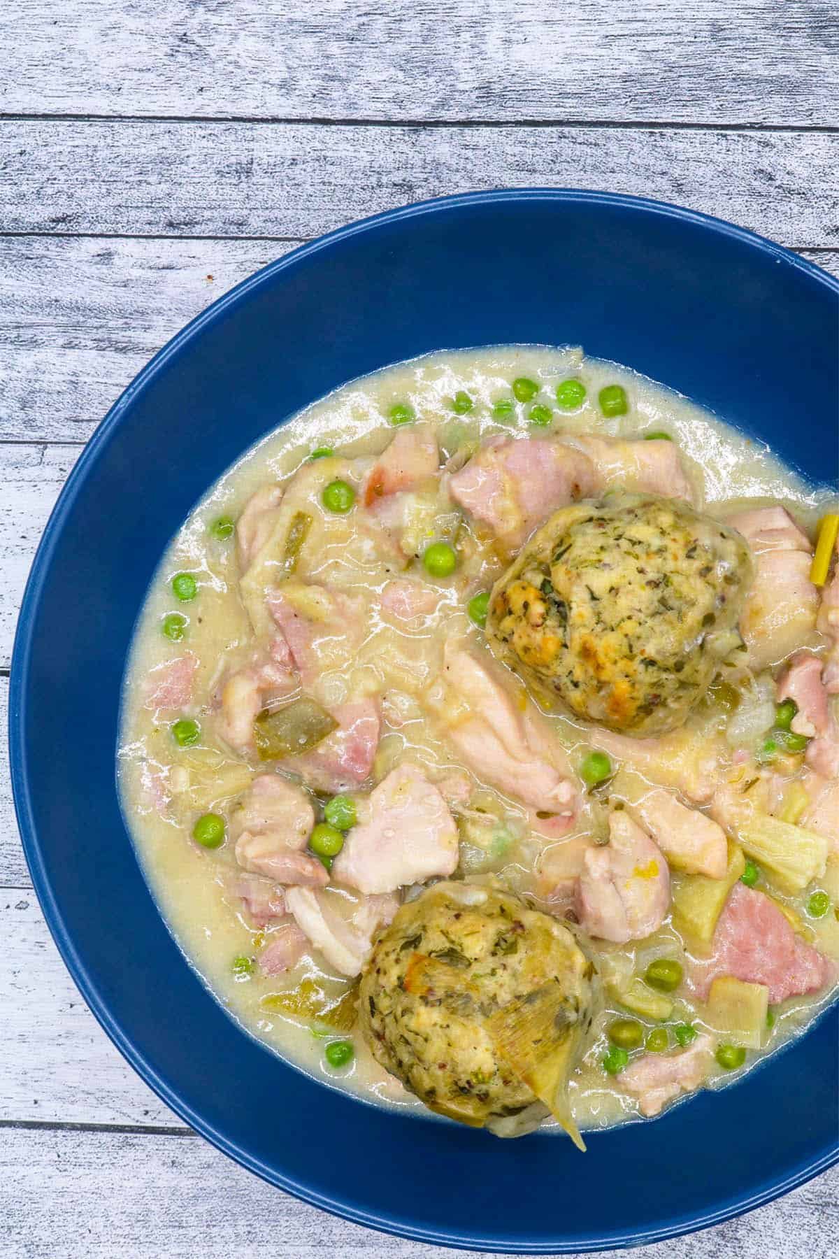 Chicken and gammon stew with buttermilk dumplings in a blue pasta bowl.