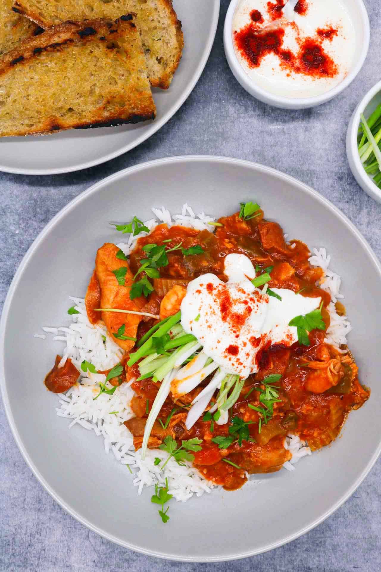 Chicken shrimp gumbo in grey bowl with rice, spring onions, soured cream and coriander