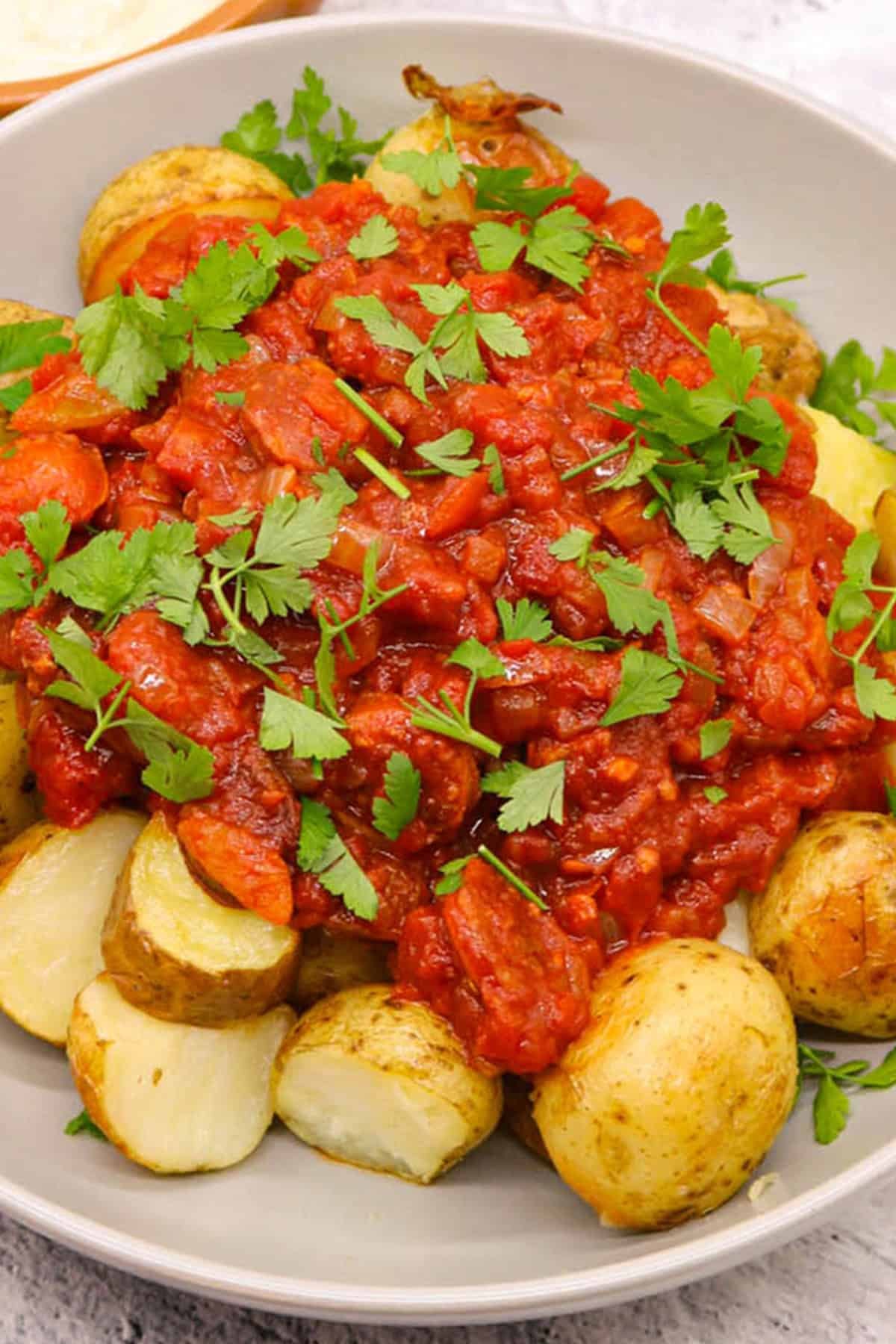 Chorizo patatas bravas in a grey serving bowl with a small dish of aioli on the side.