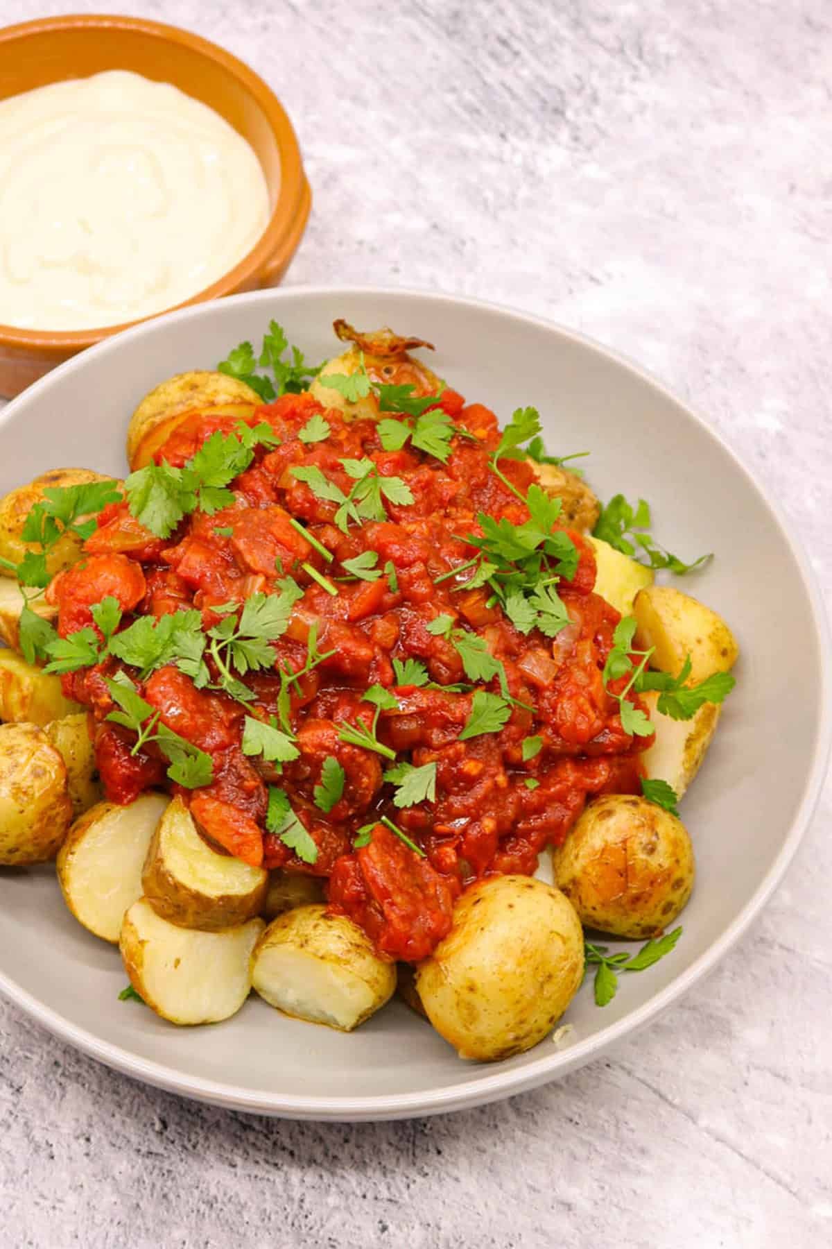 Chorizo patatas bravas in a grey serving bowl with a small dish of aioli on the side.
