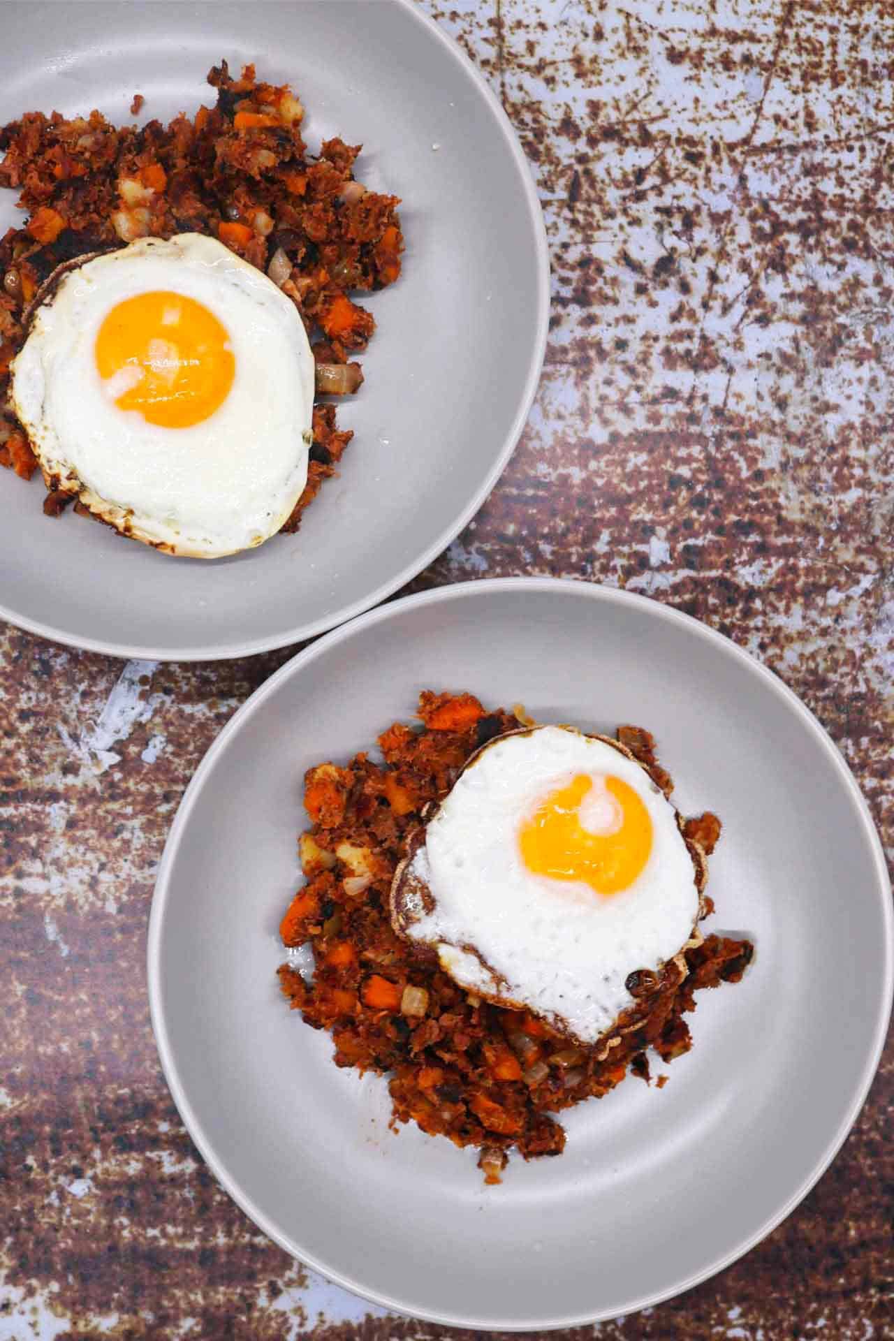 Two grey bowls with corned beef hash topped with a fried egg