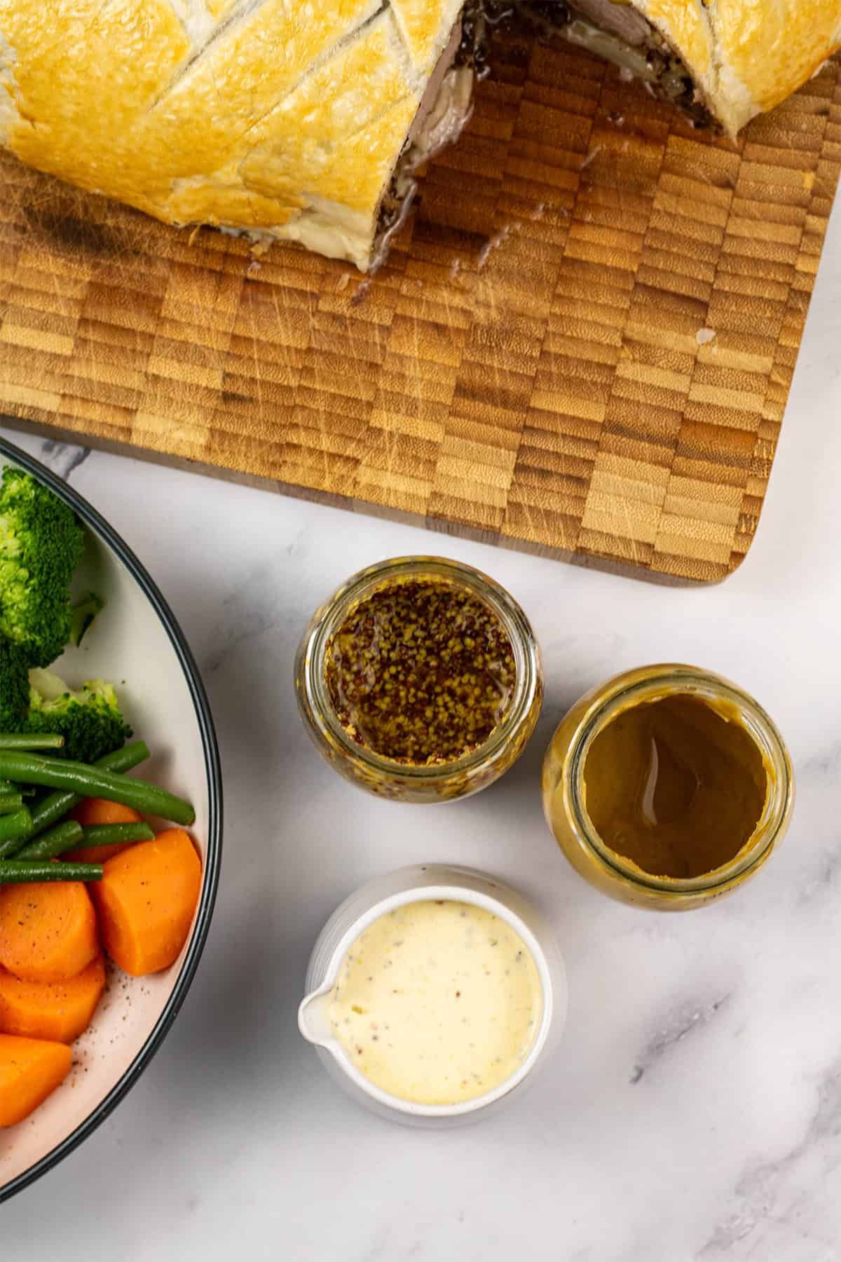 A small jug of easy mustard cream sauce with jars of wholegrain and dijon mustard on the side.