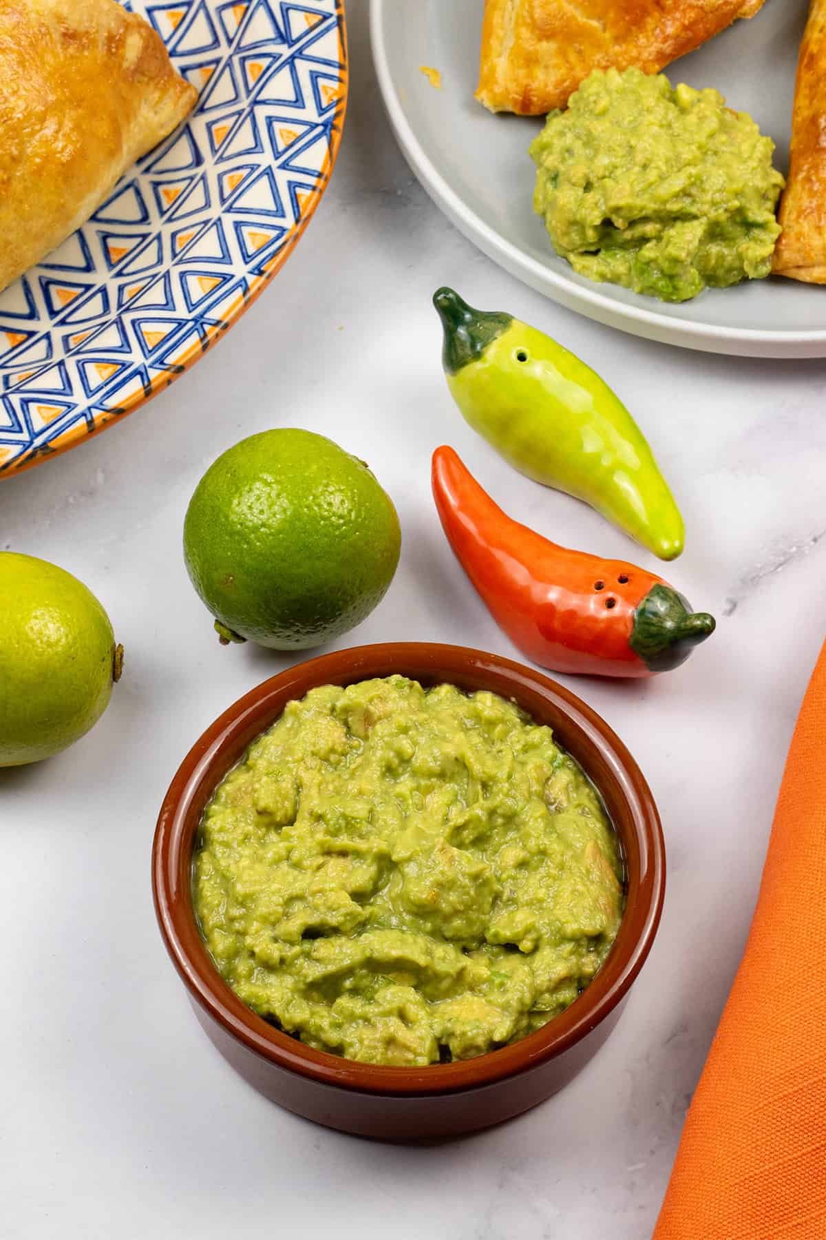 Guacamole in a terracotta serving dish with a plate of beef and chorizo empanadas on the side.