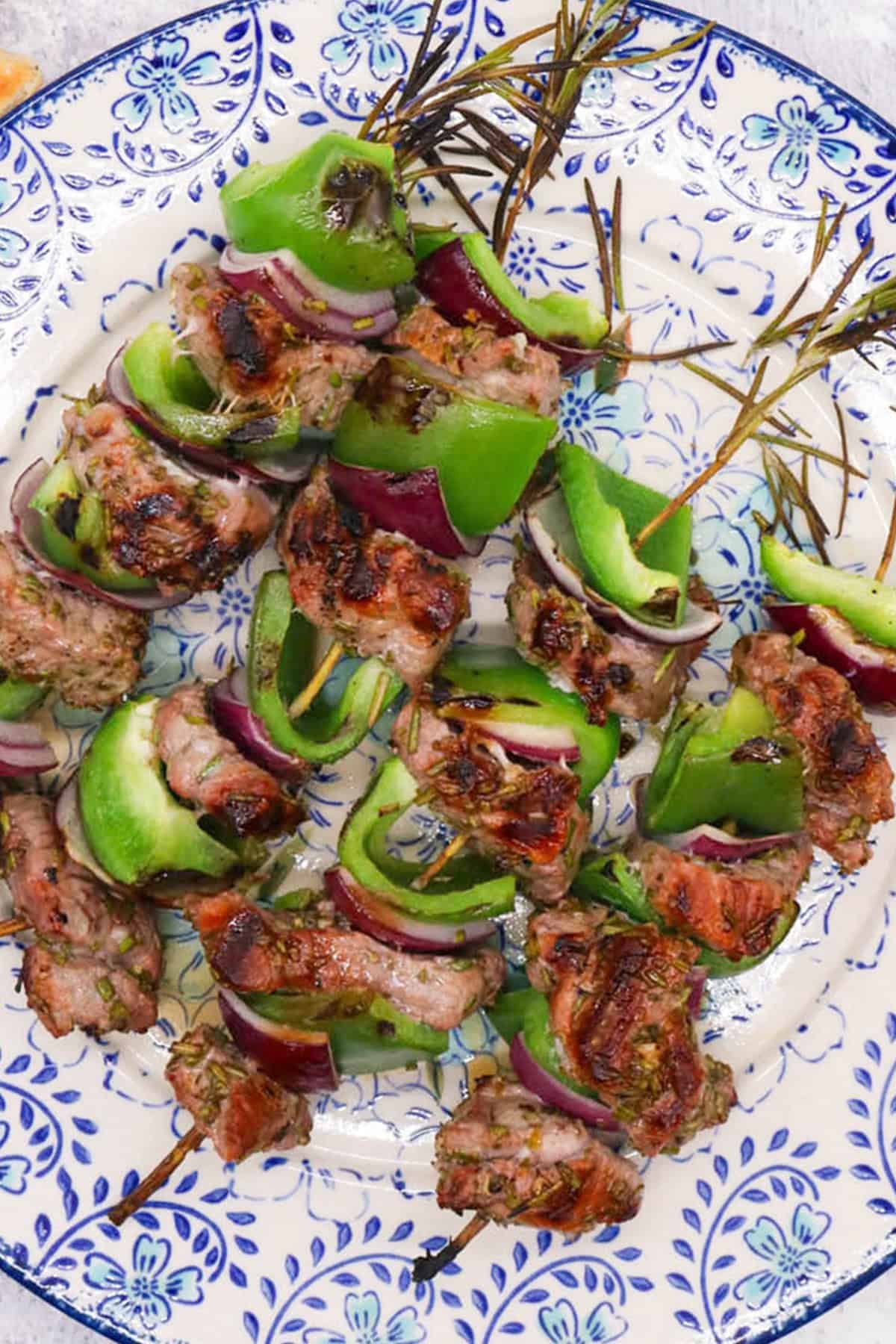Lamb with rosemary skewers on a blue and white patterned dinner plate.