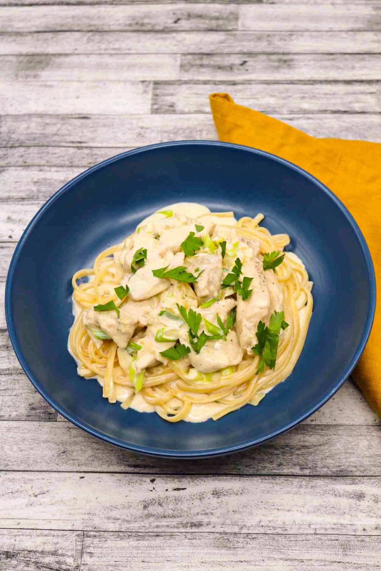 Creamy chicken linguine in blue bowl with yellow napkin at the side