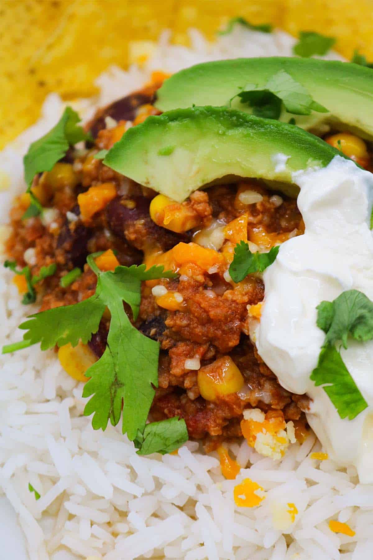 Mexican turkey chilli with rice, tortilla crisps, avocado, coriander and soured cream in bowl