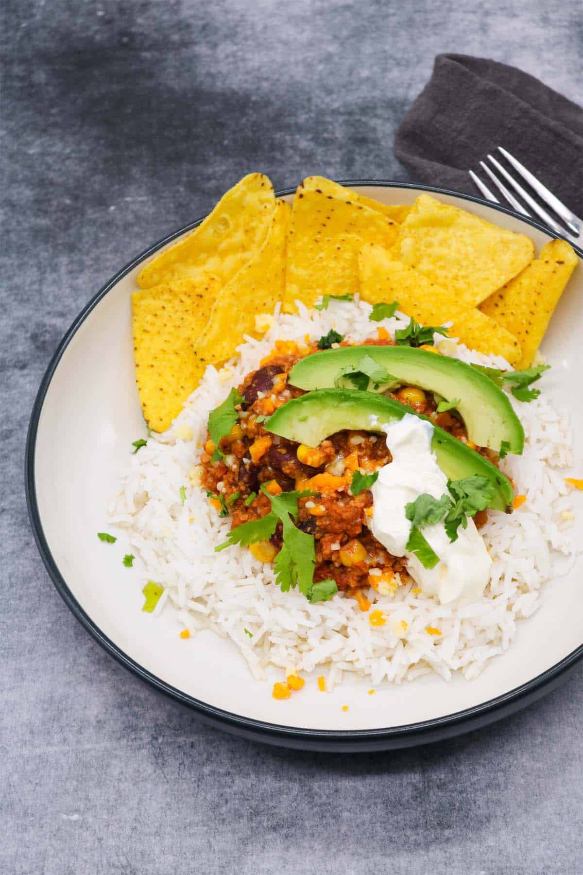 Mexican turkey chilli with rice, tortilla crisps, avocado, coriander and soured cream in bowl