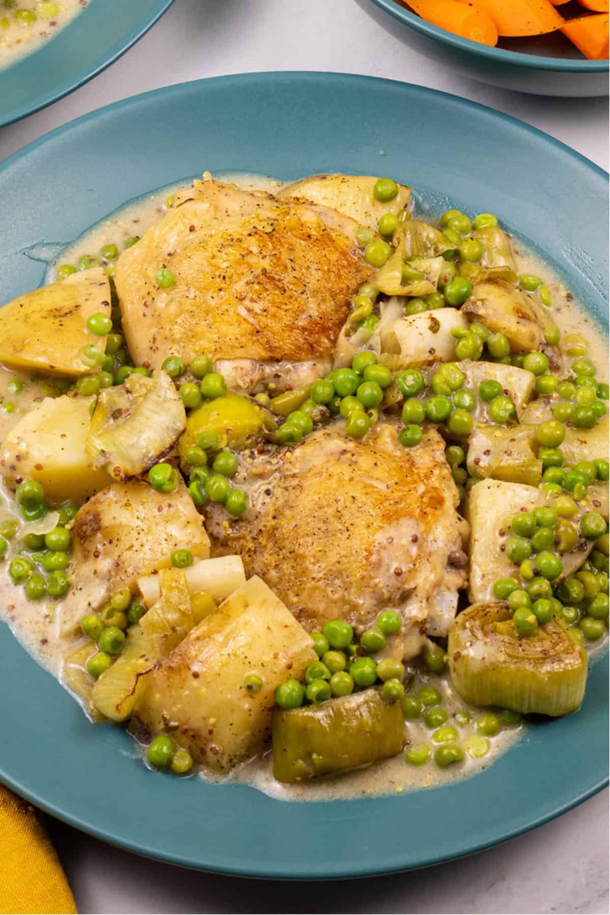 A close up portion of mustard chicken and leek one-pot on a teal dinner plate.