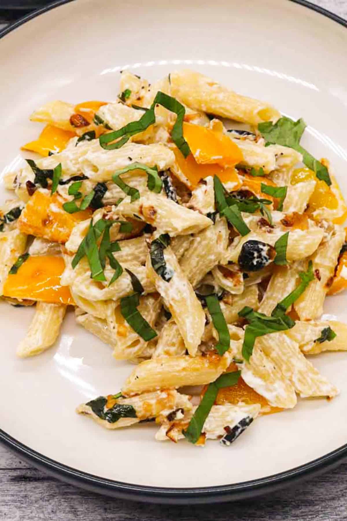 Close photo of penne with peppers and goats cheese in a black and cream pasta bowl.