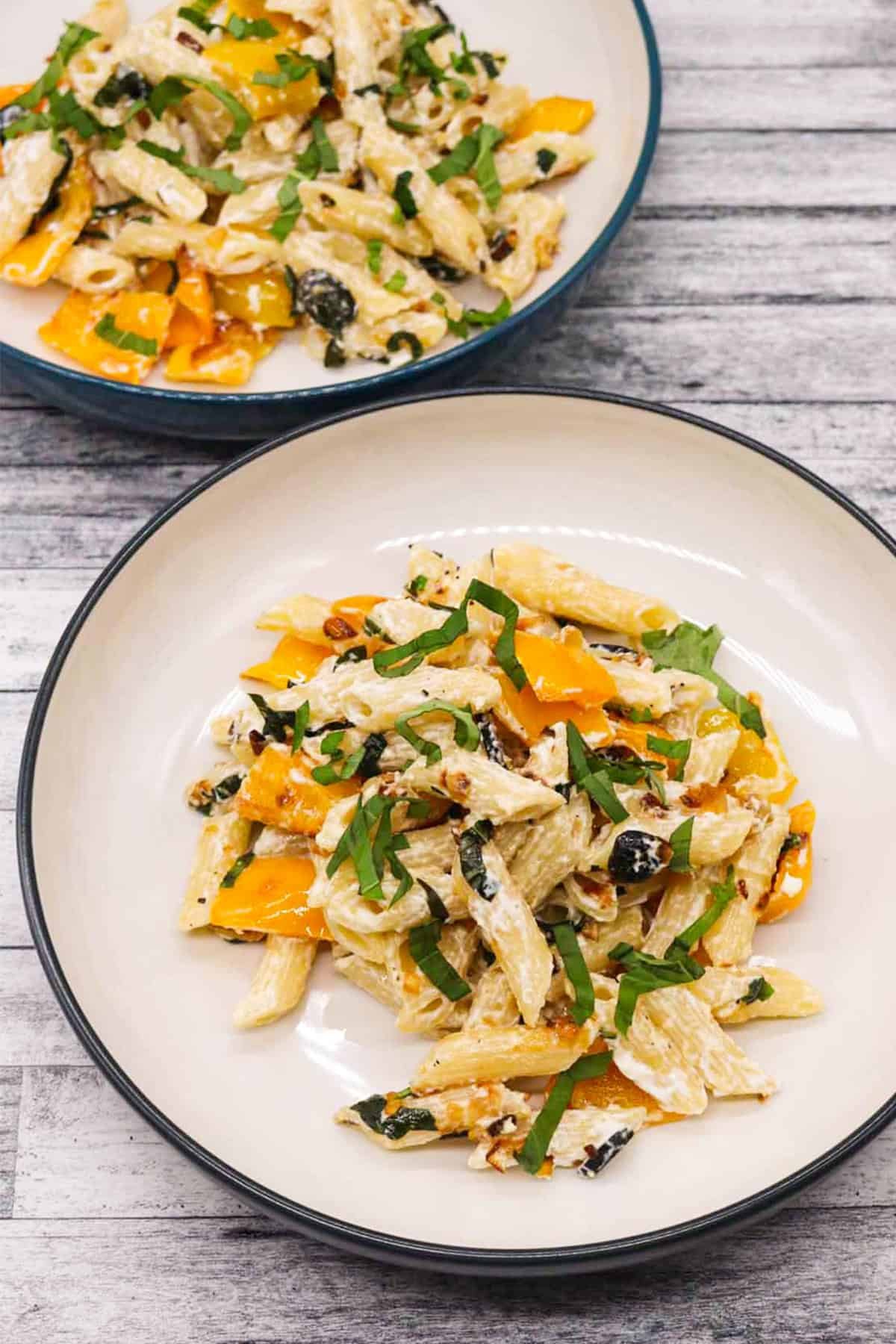 Two bowls of penne with peppers and goats cheese.