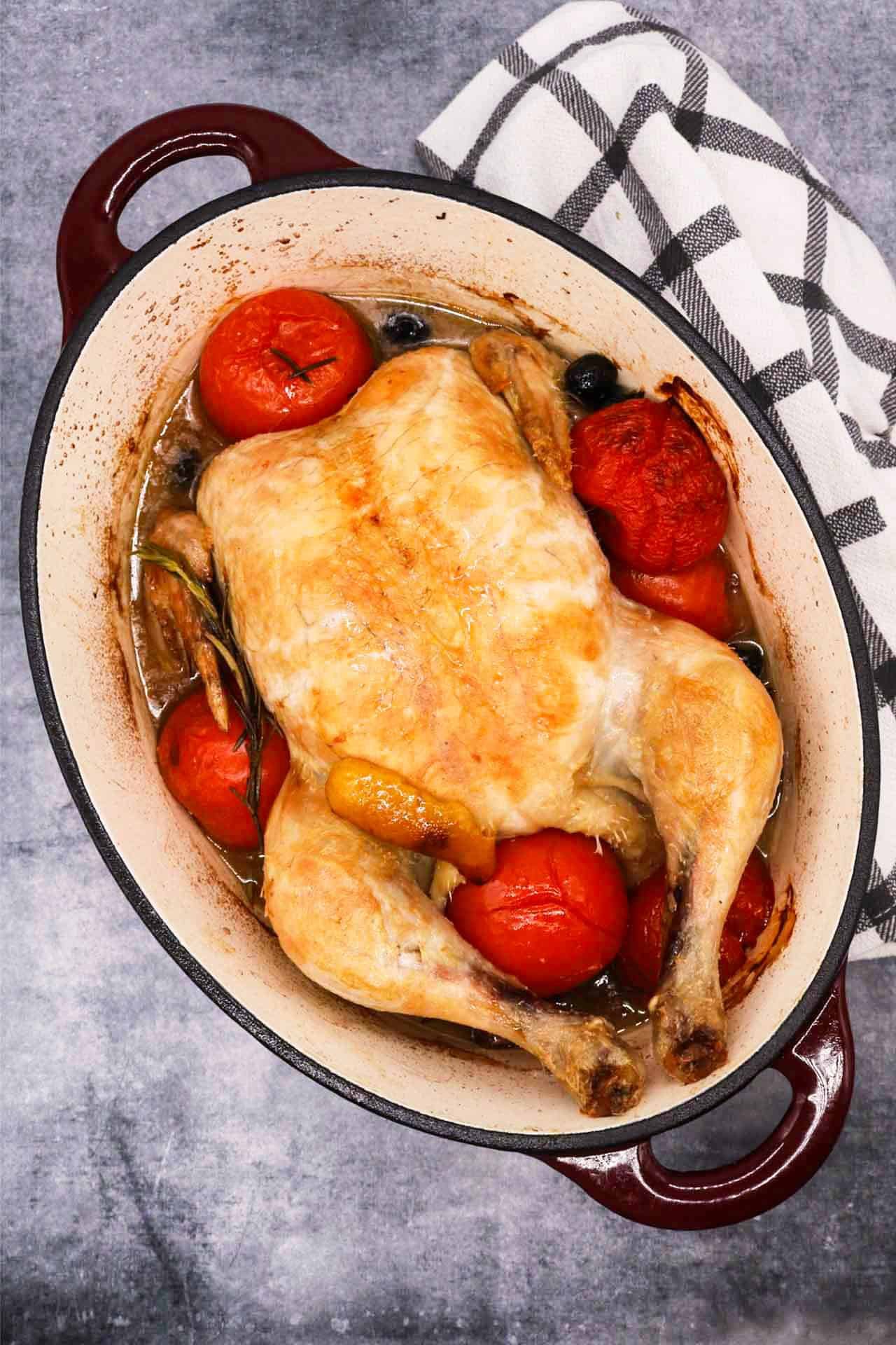 Whole chicken in oval casserole dish with tomatoes and rosemary