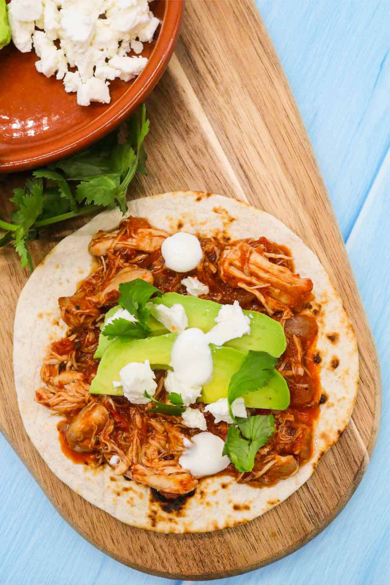 Chicken tinga on flour tortilla with avocado and cheese on wooden board