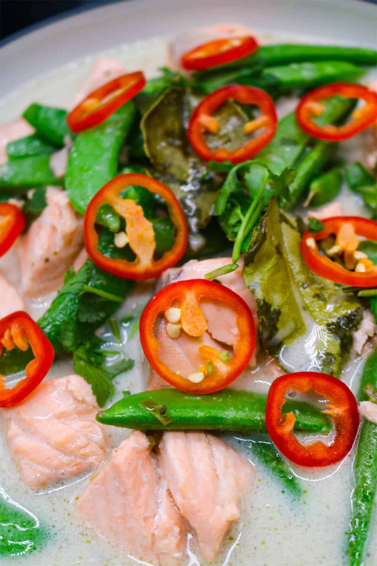 Thai green salmon curry in bowl with green vegetables and sliced red chilli
