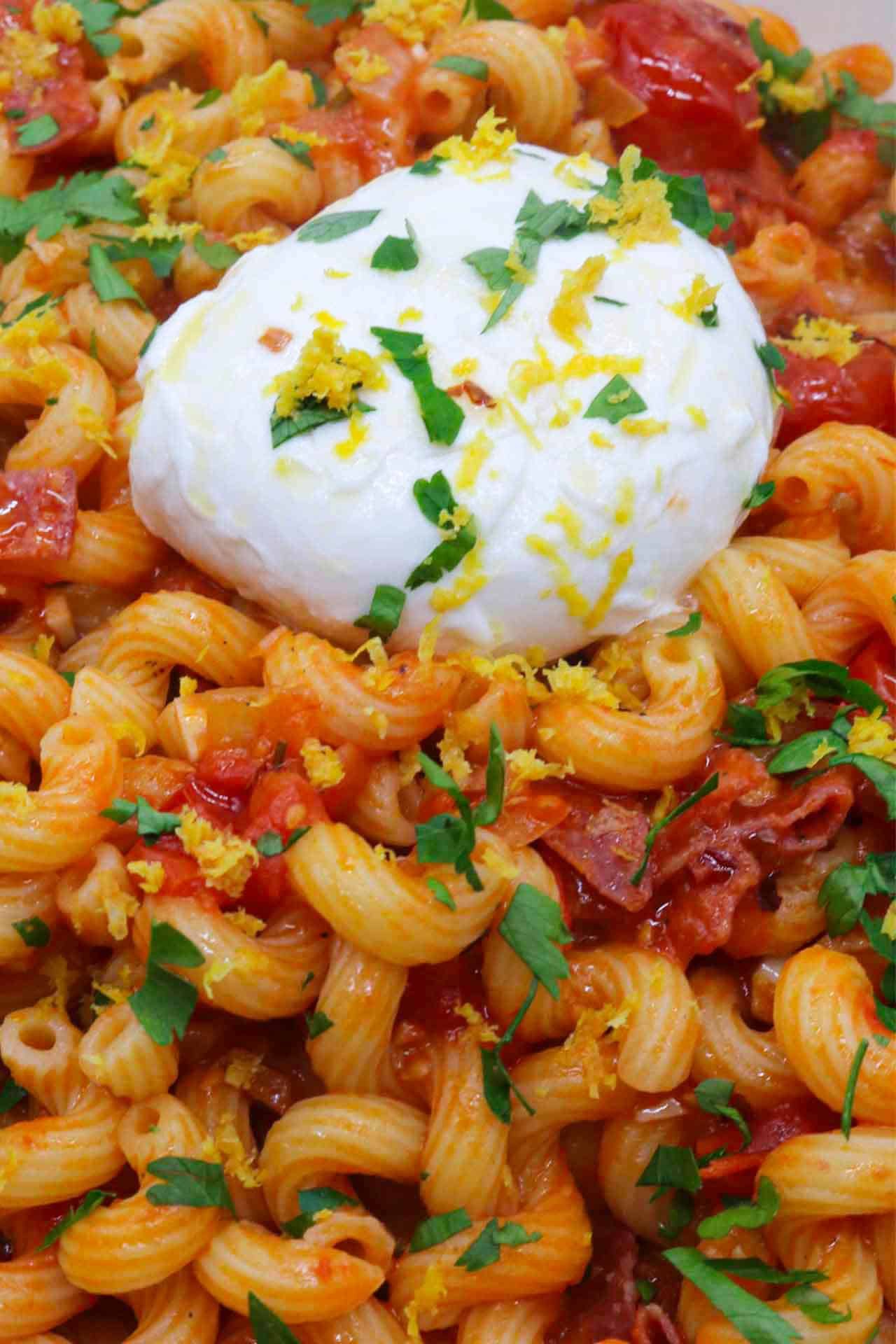 Tomato salami pasta with large ball of burrata in rectangle serving dish