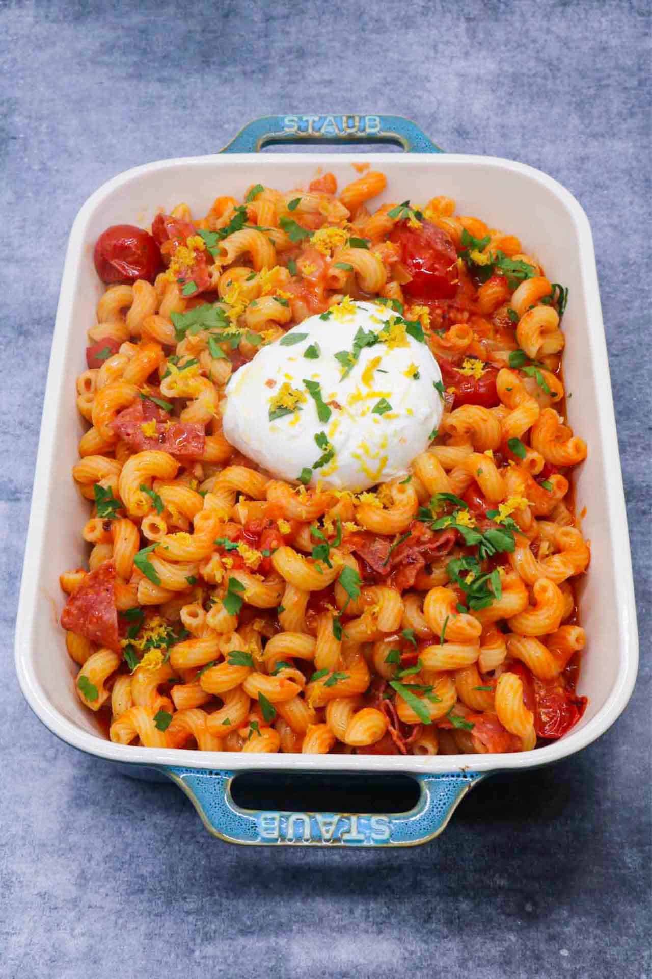 Tomato salami pasta with large ball of burrata in rectangle serving dish