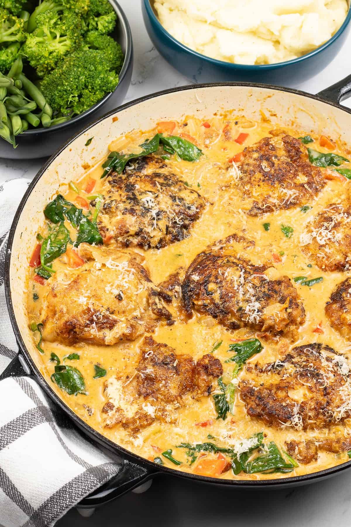Tuscan chicken in large round casserole dish with bowls of green beans and broccoli, and mashed potatoes on the side.