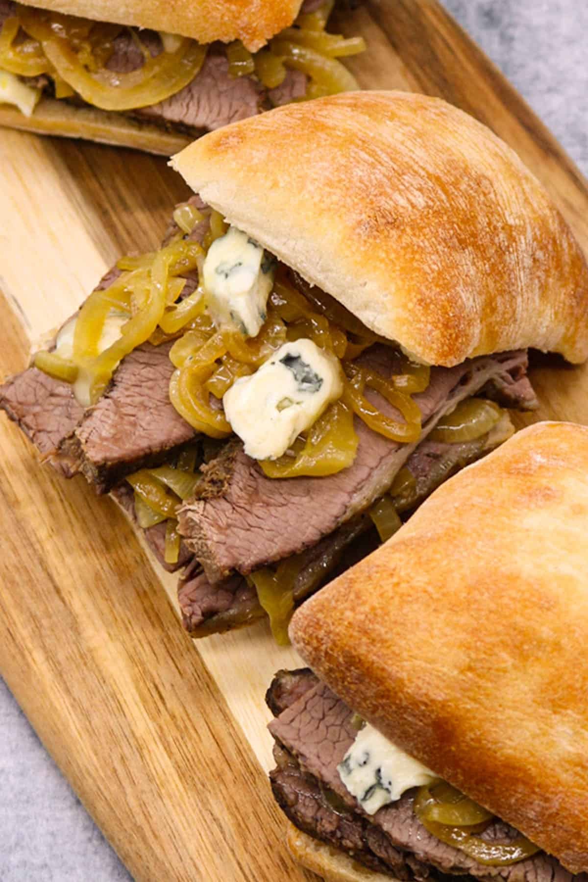 Three Brisket sandwiches with beer onions and blue cheese on a board