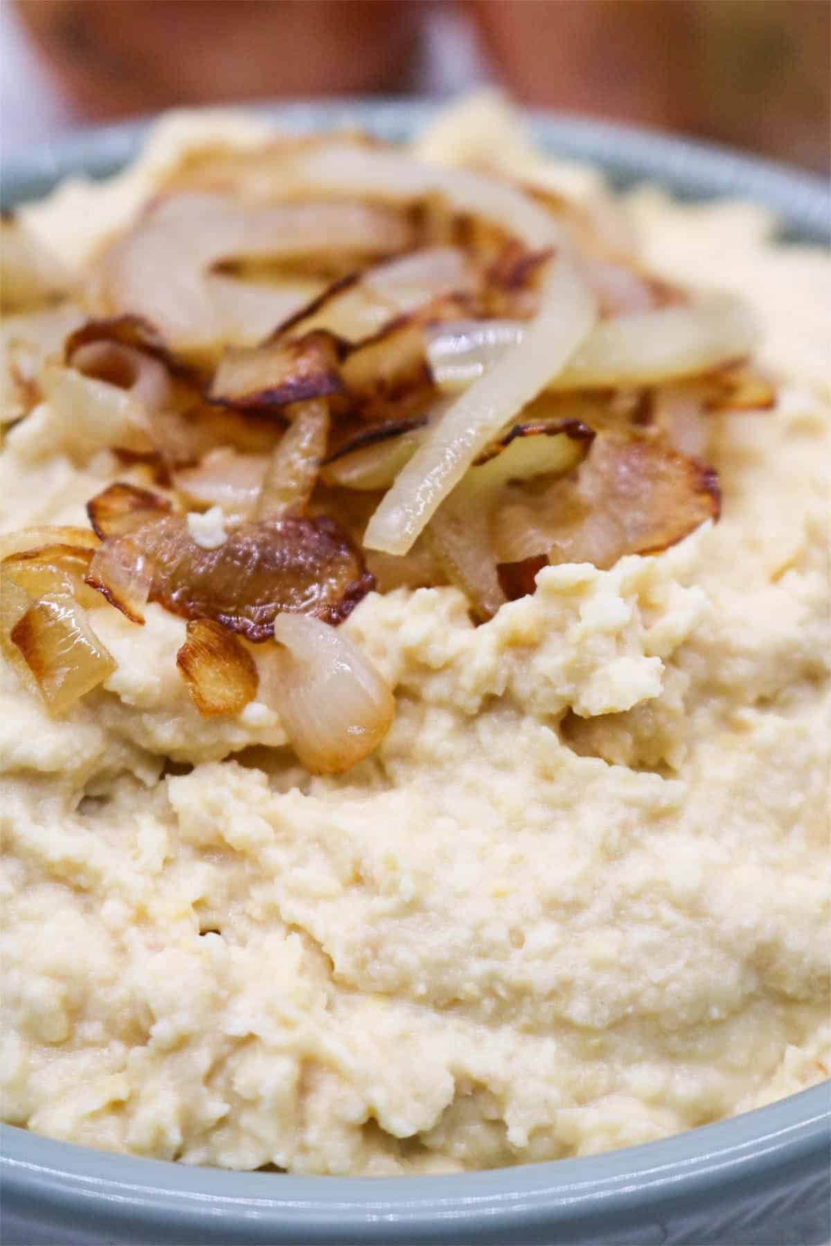Caramelised onion houmous in bowl with onions on top and raw onions in background