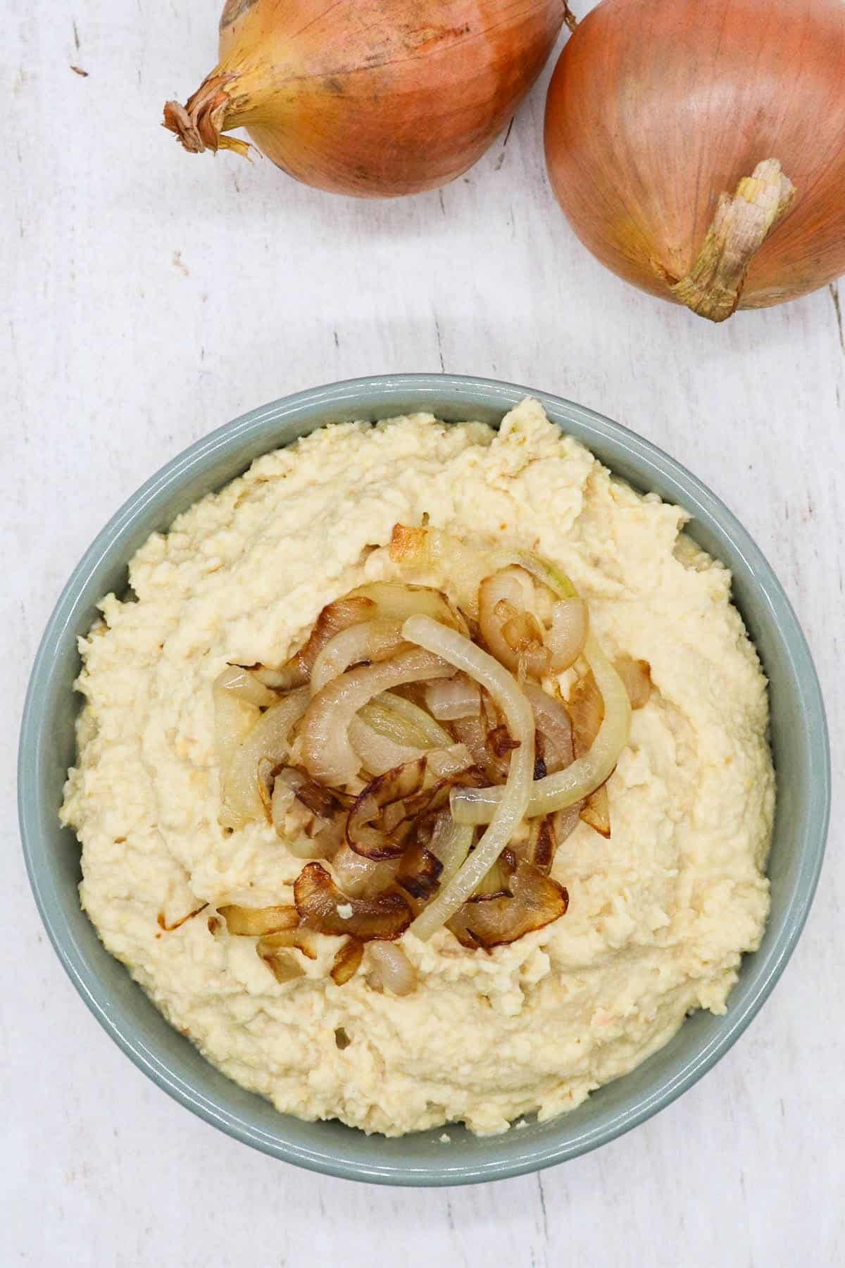 Caramelised onion houmous in bowl with onions on top and raw onions in background
