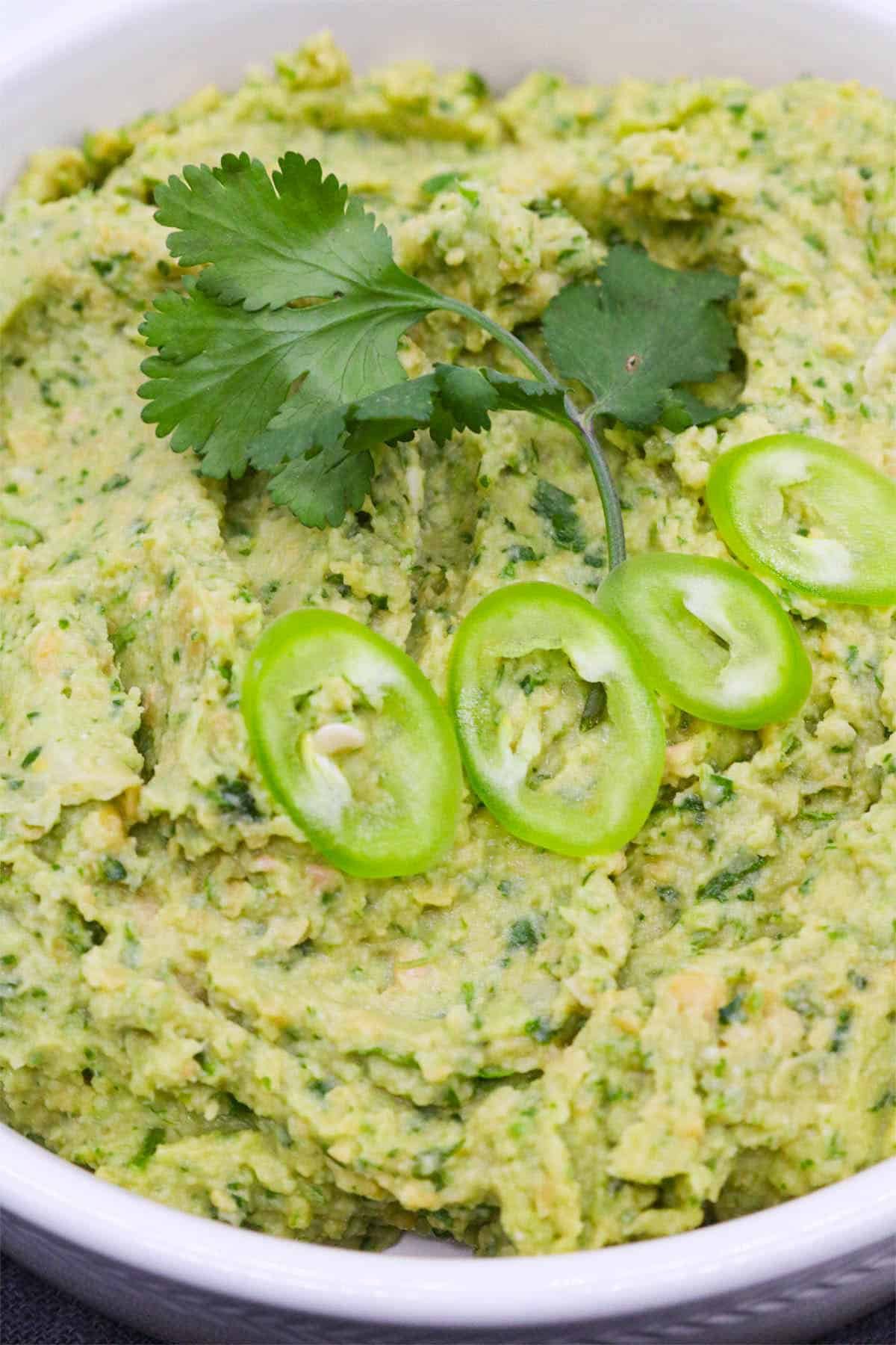 Coriander and green chilli humous in bowl with coriander and sliced chillis on top