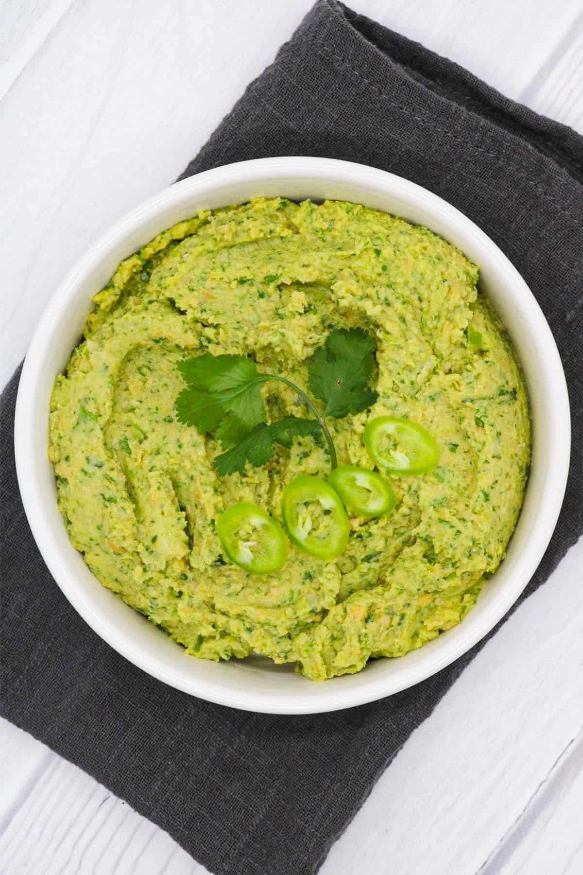 Coriander and green chilli humous in bowl with coriander and sliced chillis on top