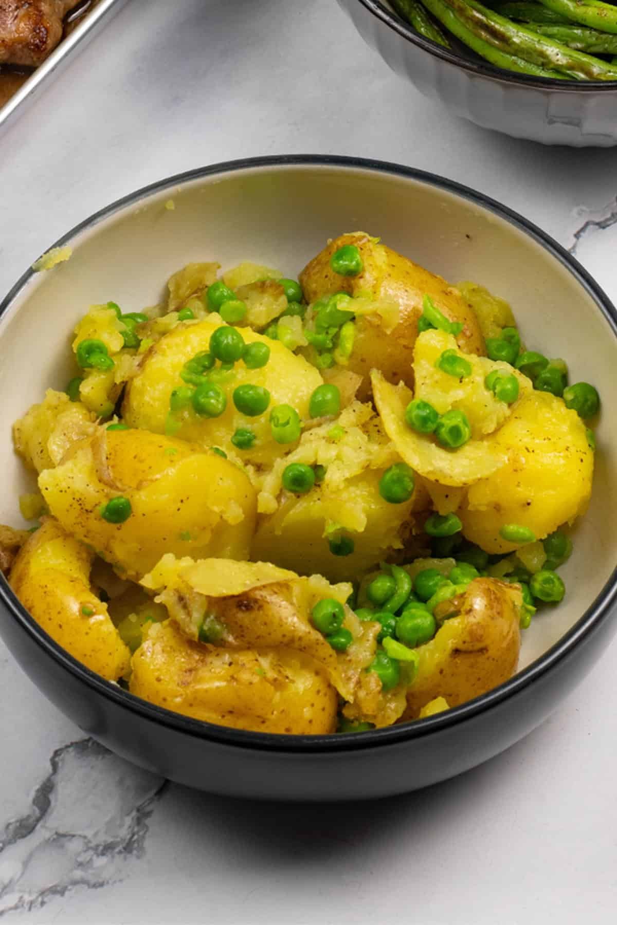 Easy crushed potatoes with peas in a black and cream serving bowl.