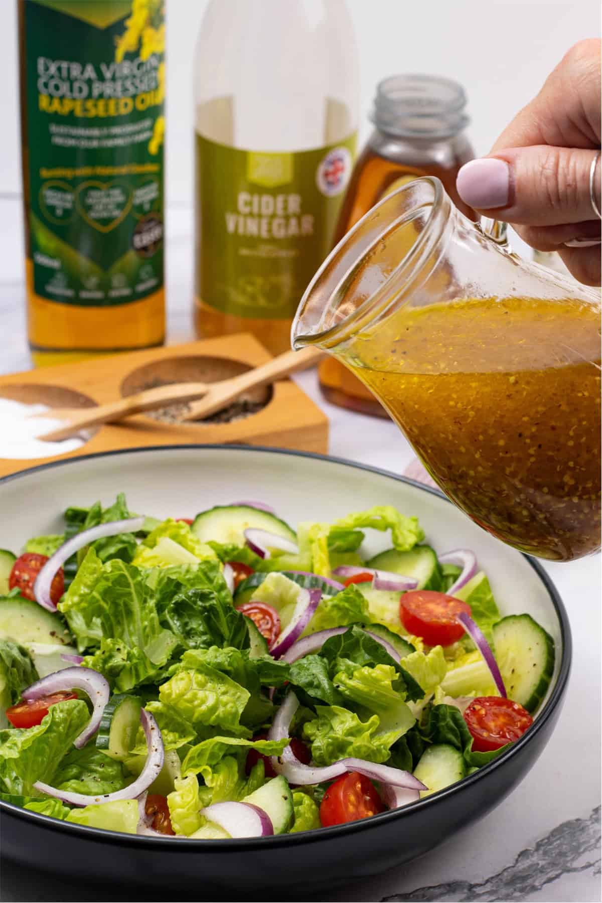 Honey mustard dressing in a small glass jug with a bowl of salad and the ingredients in the background.
