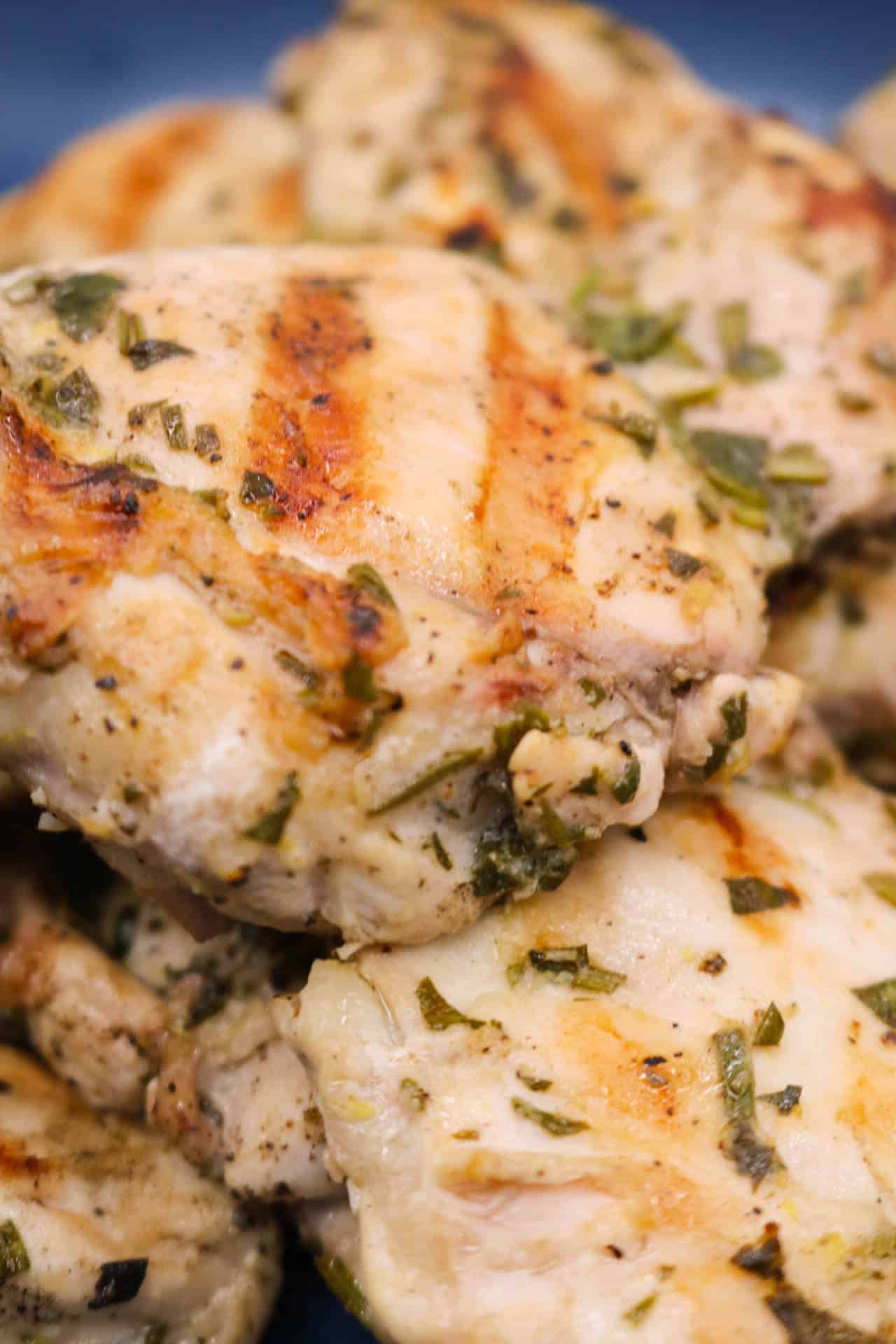 Lemon herb chicken thighs in blue bowl with mint and rosemary to the side