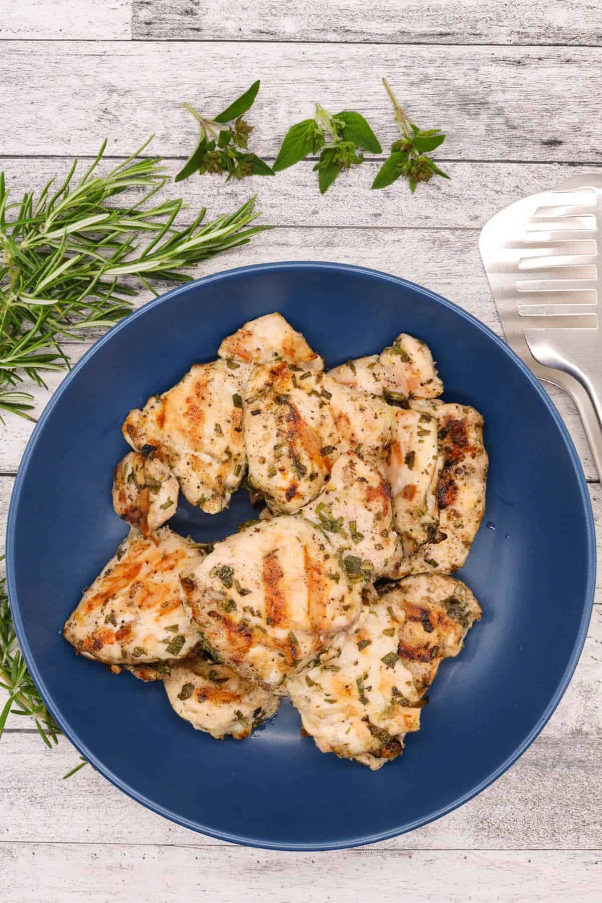 Lemon herb chicken thighs in blue bowl with mint and rosemary to the side