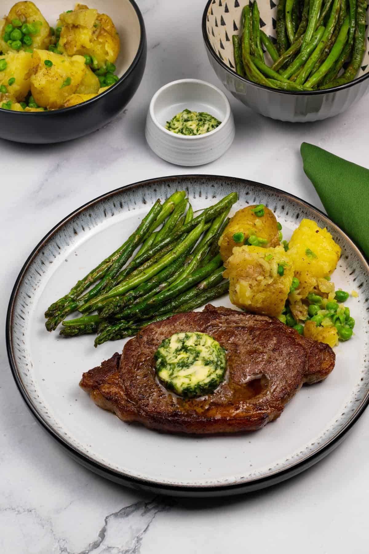 A perfect sirloin steak plated with crushed potatoes and peas, sautéed asparagus and green beans, and wild garlic and rosemary butter.