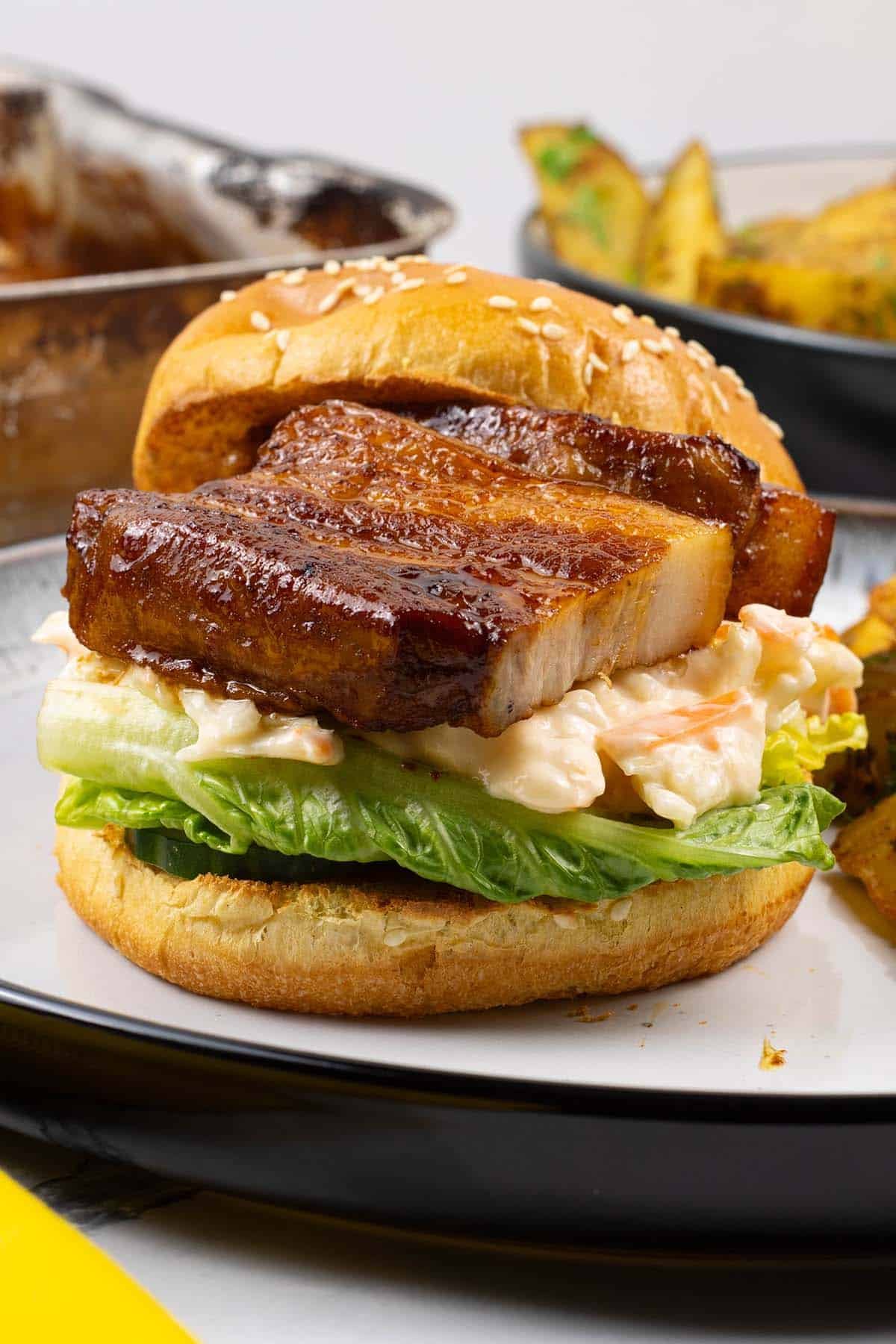 Pork belly slices in BBQ sauce in a brioche bun with salad leaves and coleslaw, with herby garlic butter potato wedges.