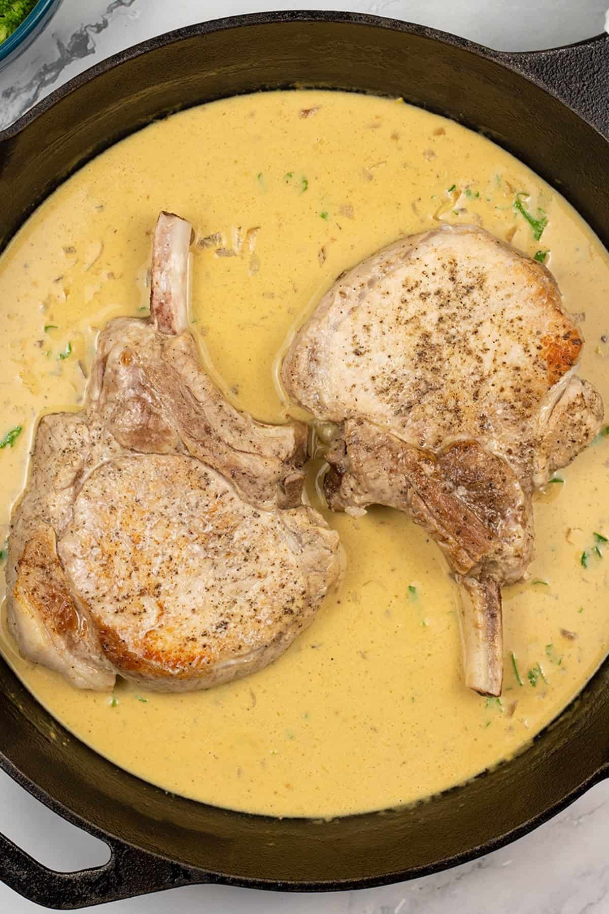 2 pork chops with dijon sauce in a skillet pan.
