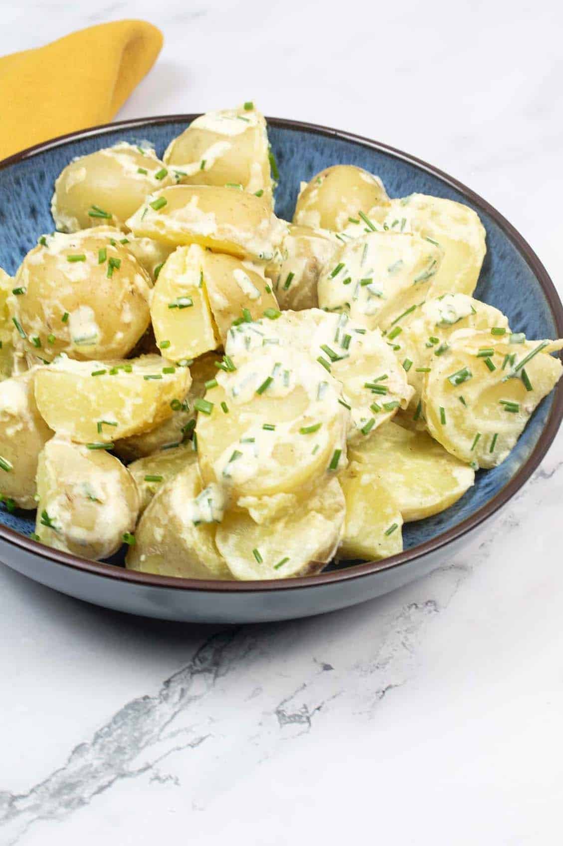 Potato salad in a blue patterned bowl with mustard napkin in the background.