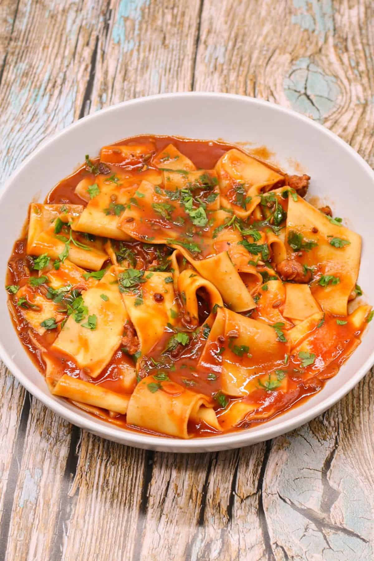 Sausage and pappardelle pasta in a light grey pasta bowl.