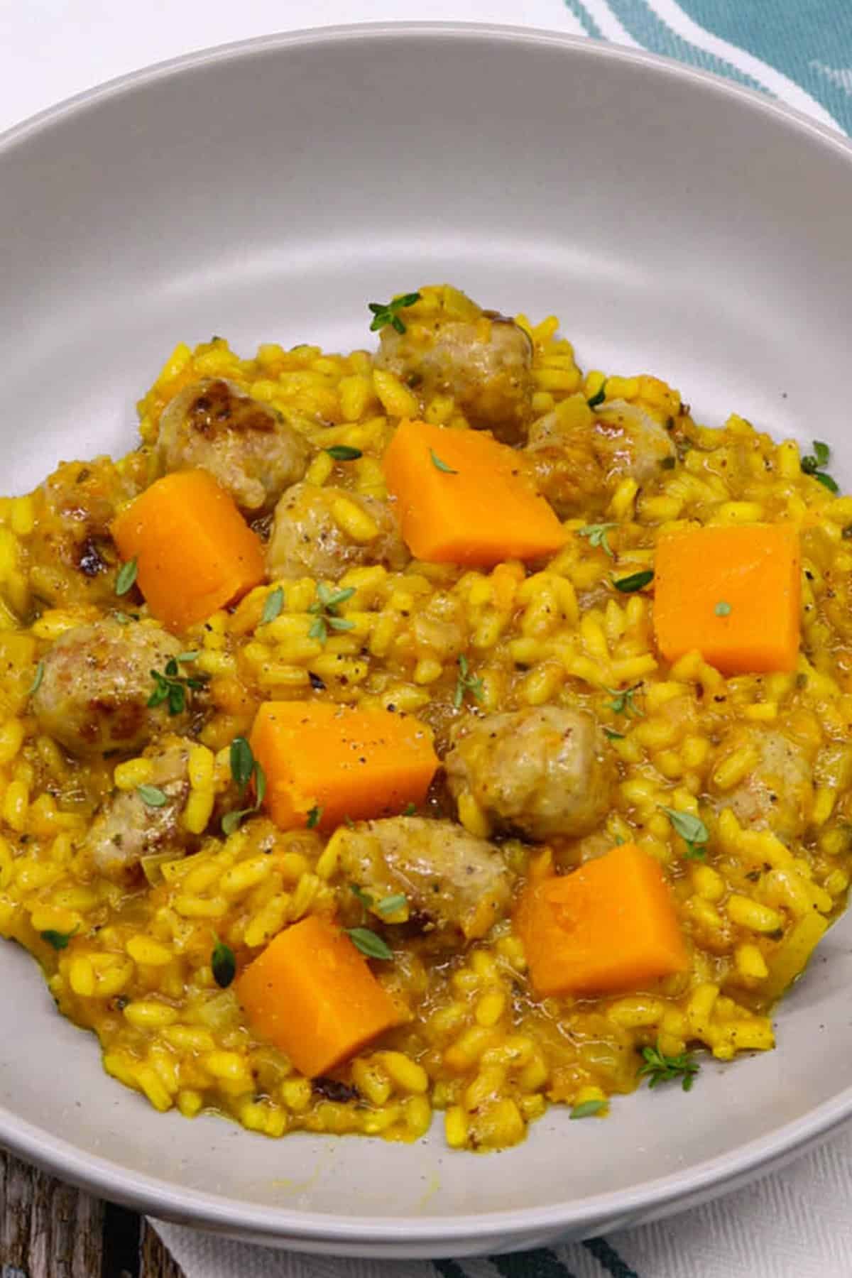 A portion of sausage and squash risotto in a grey bowl sitting on top of a teal green and white towel.
