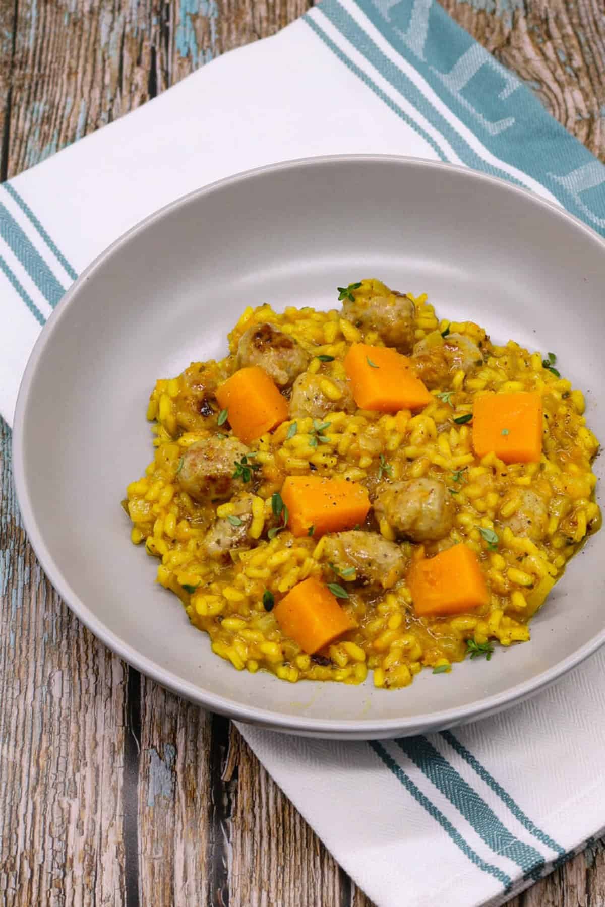 A portion of sausage and squash risotto in a grey bowl sitting on top of a teal green and white towel.