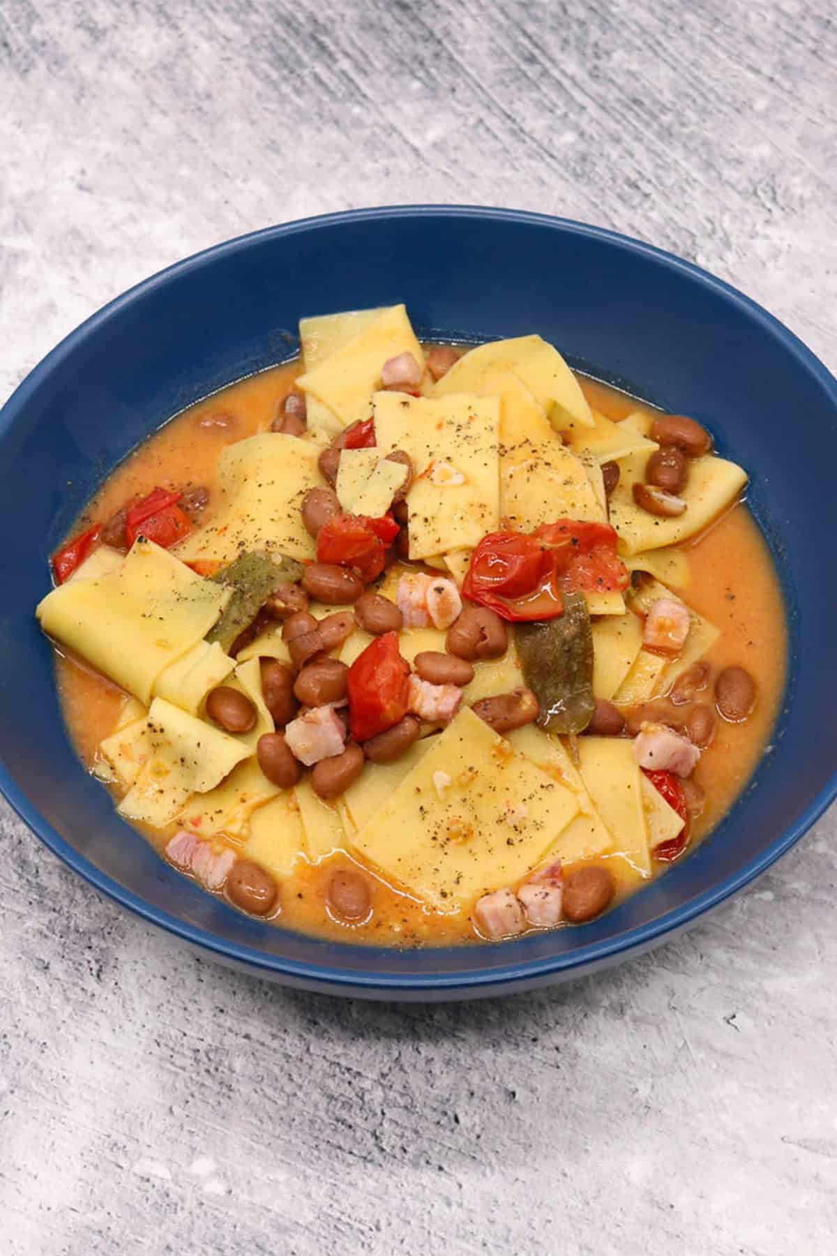 A portion of smoked pancetta and bean pasta in a dark blue bowl.