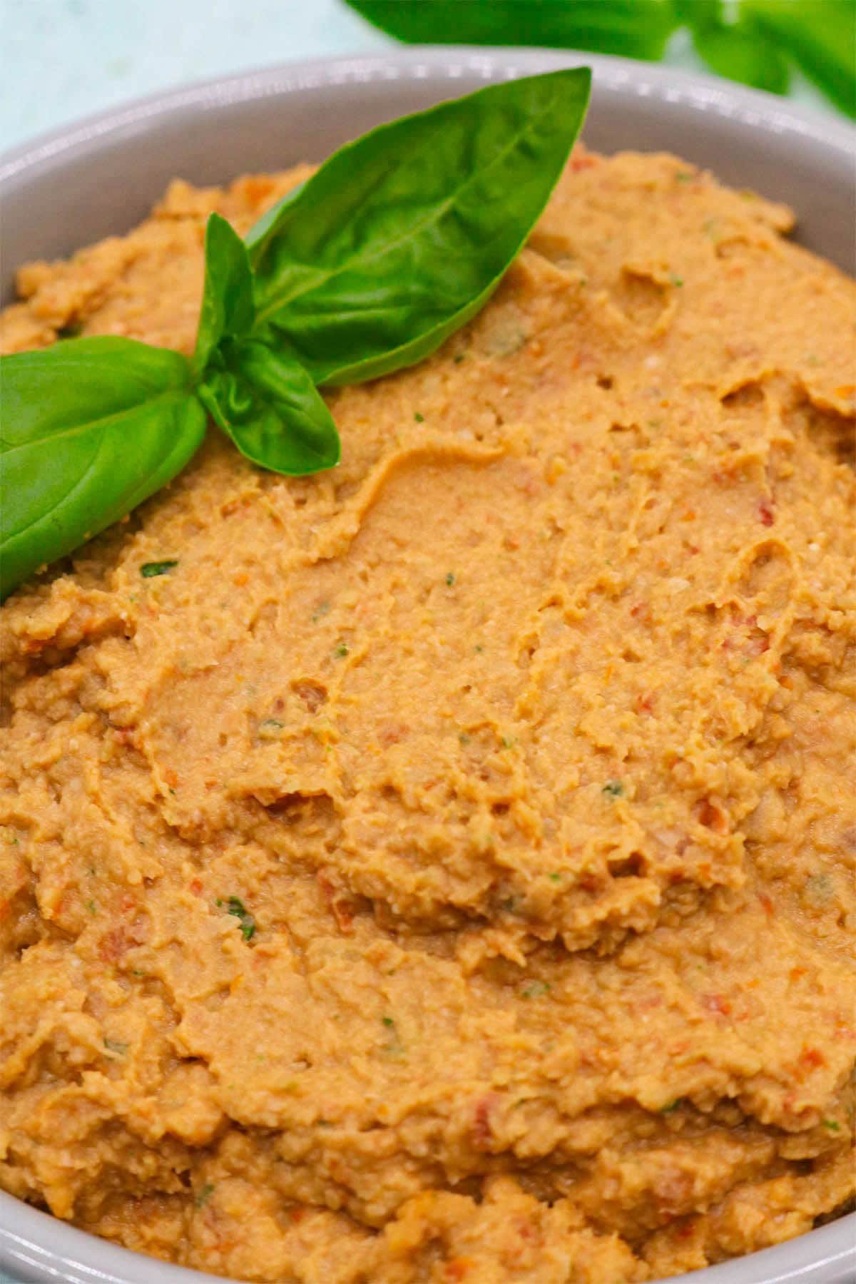 Sun dried tomato and basil humous in bowl with basil leaves