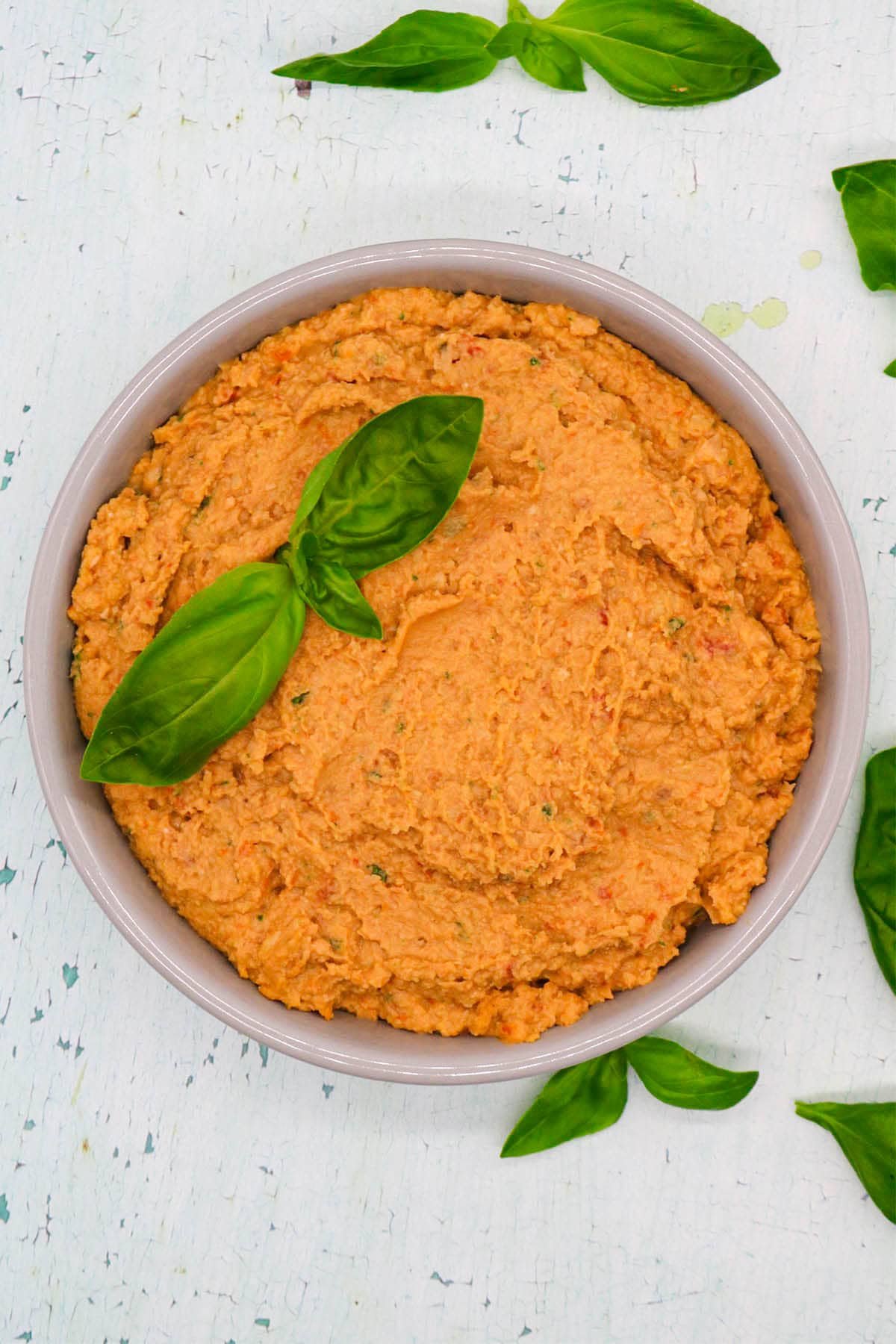 Sun dried tomato and basil humous in bowl with basil leaves
