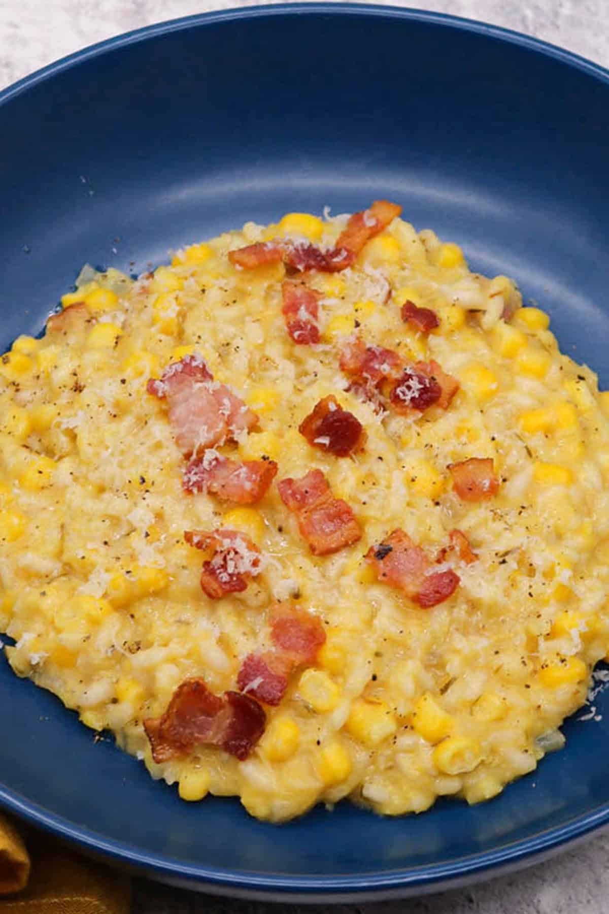 Close up of a portion of sweetcorn and bacon risotto in a dark blue bowl.