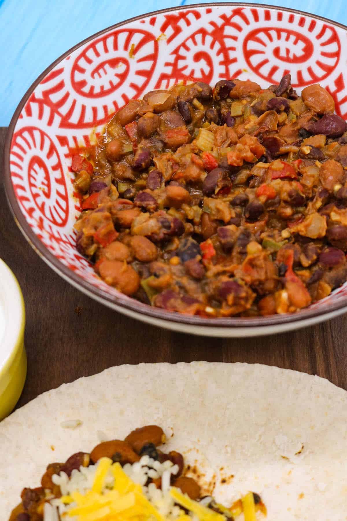 Veggie chilli on flour tortilla with rice jalapeños and cheese on wooden board