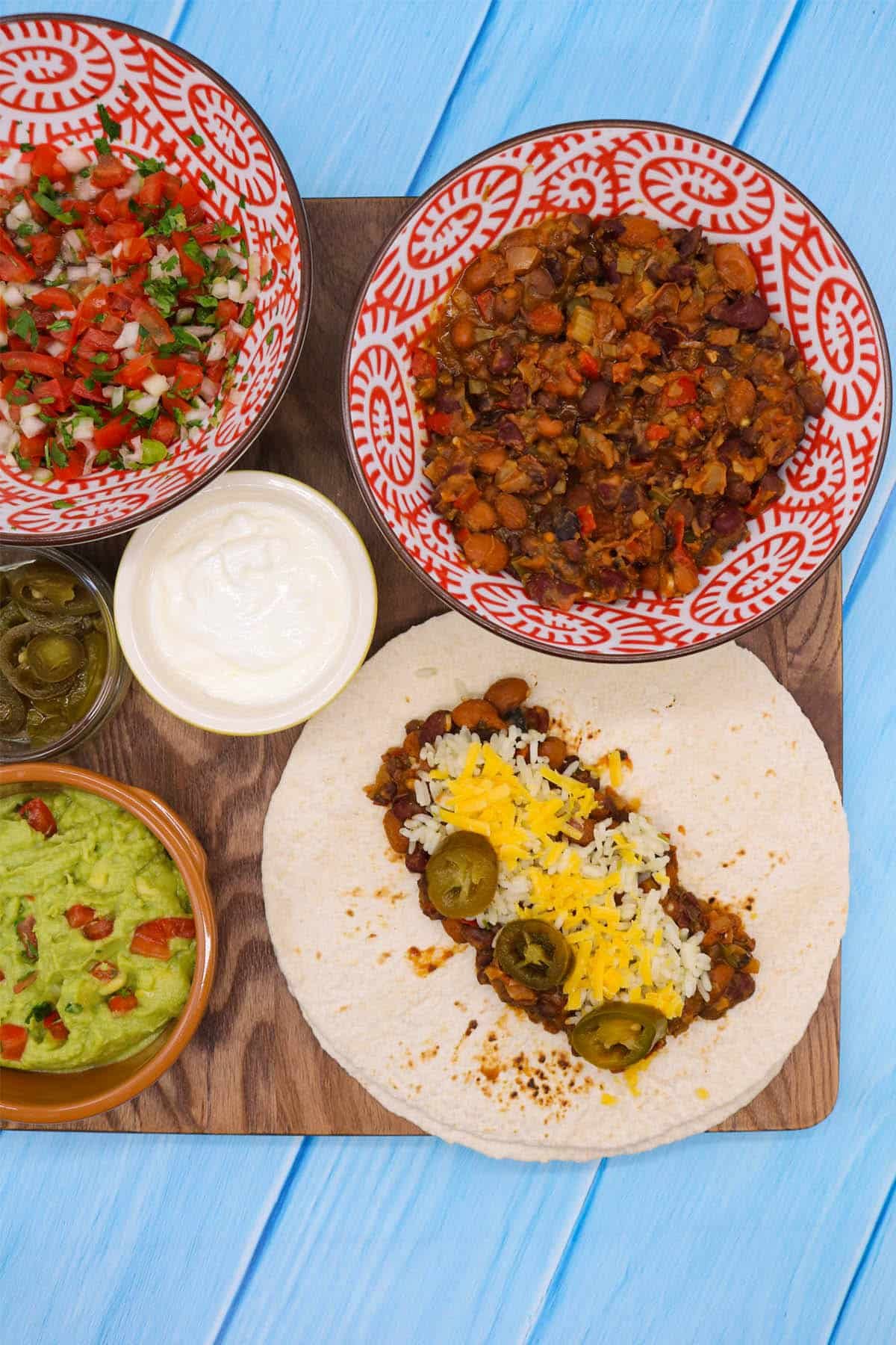 Veggie chilli on flour tortilla with rice jalapeños and cheese on wooden board