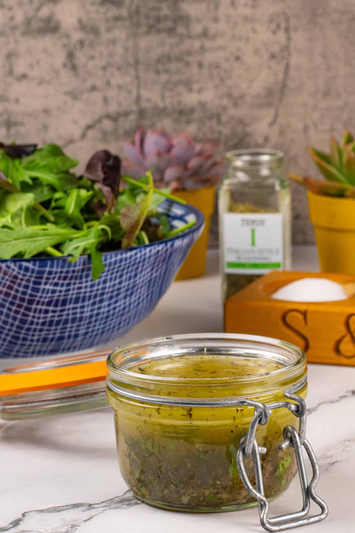 Zesty Italian-style dressing in a jar with a bowl of mixed leaf salad on the side.
