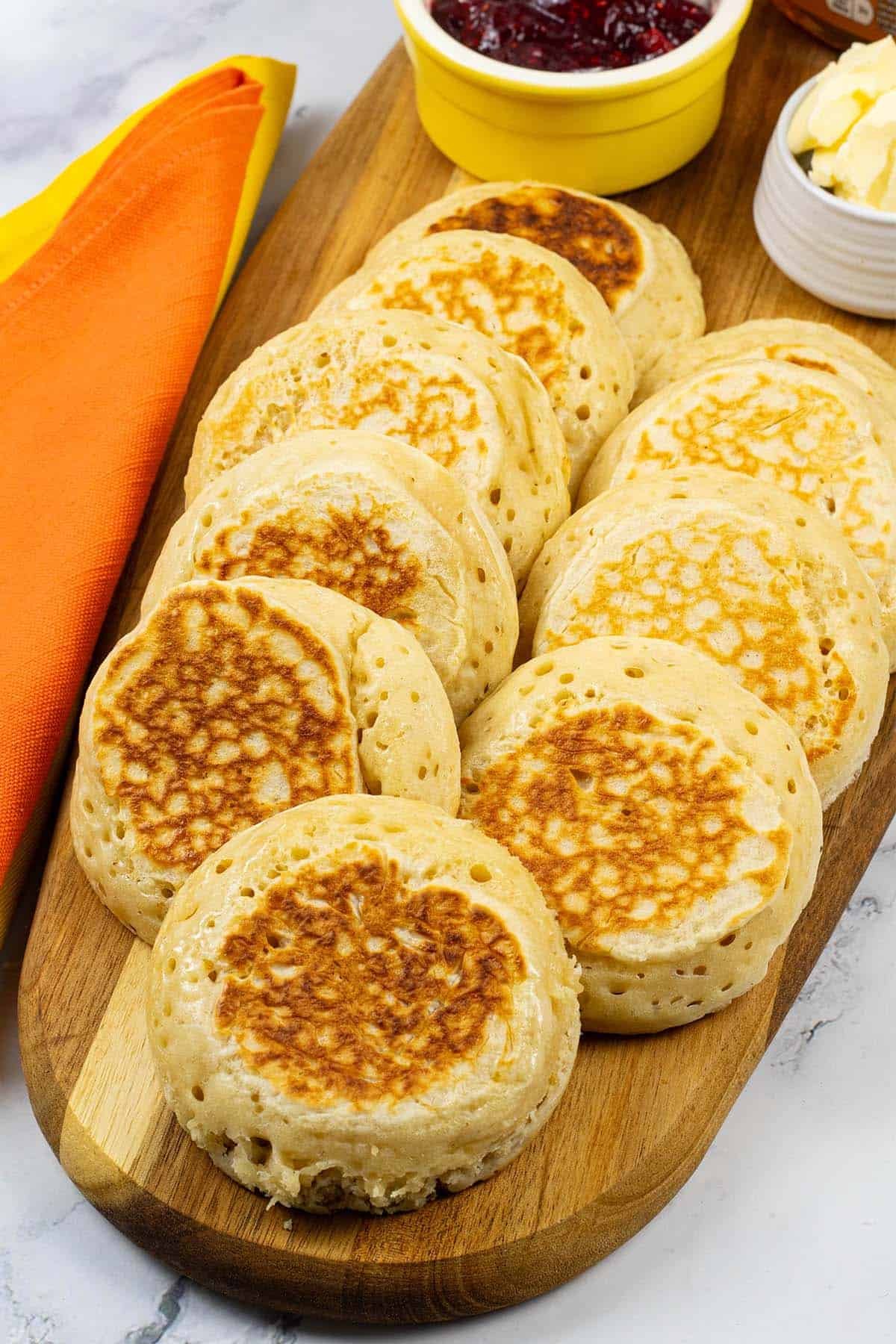 Homemade crumpets on a board with dishes of jam and butter.