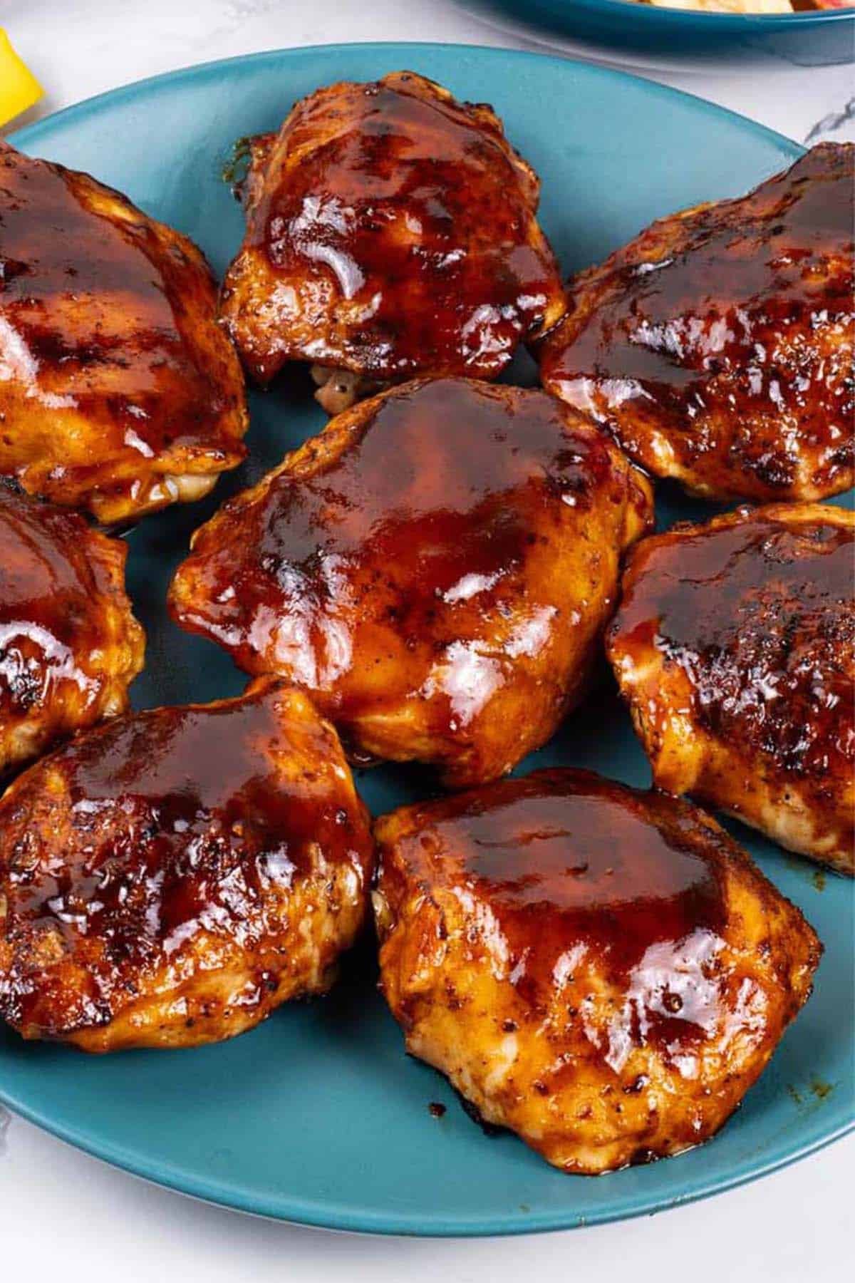 Close up of juicy BBQ chicken thighs on a teal plate.