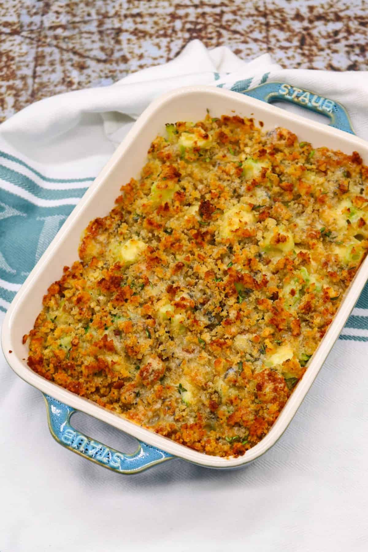 Broccoli and stilton crumble in a rectangle Staub oven dish sitting on a white and teal towel.
